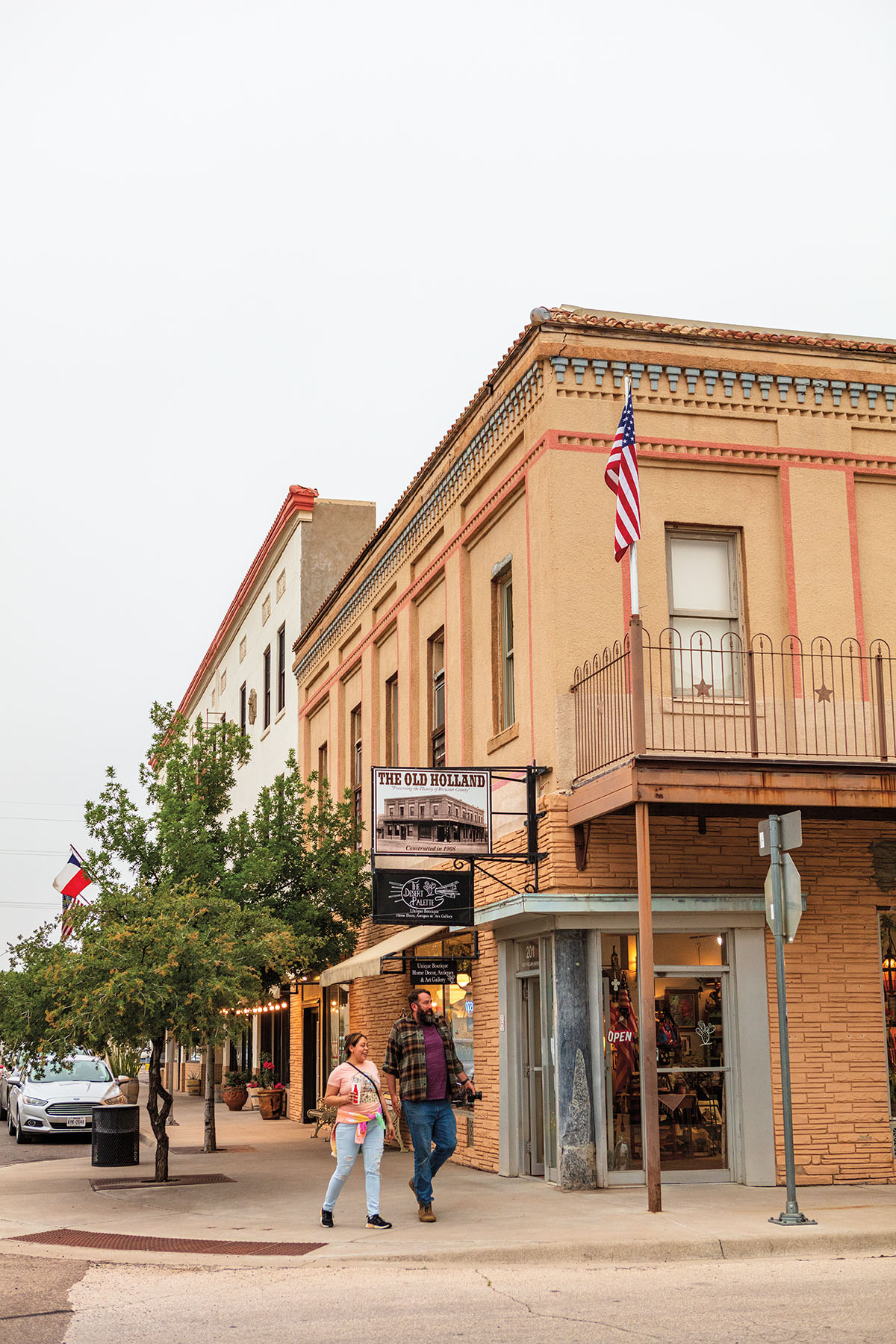 Two people walk down a street next to a gallery in a historic downtown