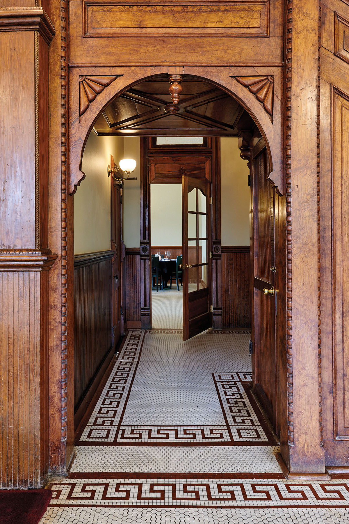 An ornate wooden entryway with wooden doors and precise white and brown tile