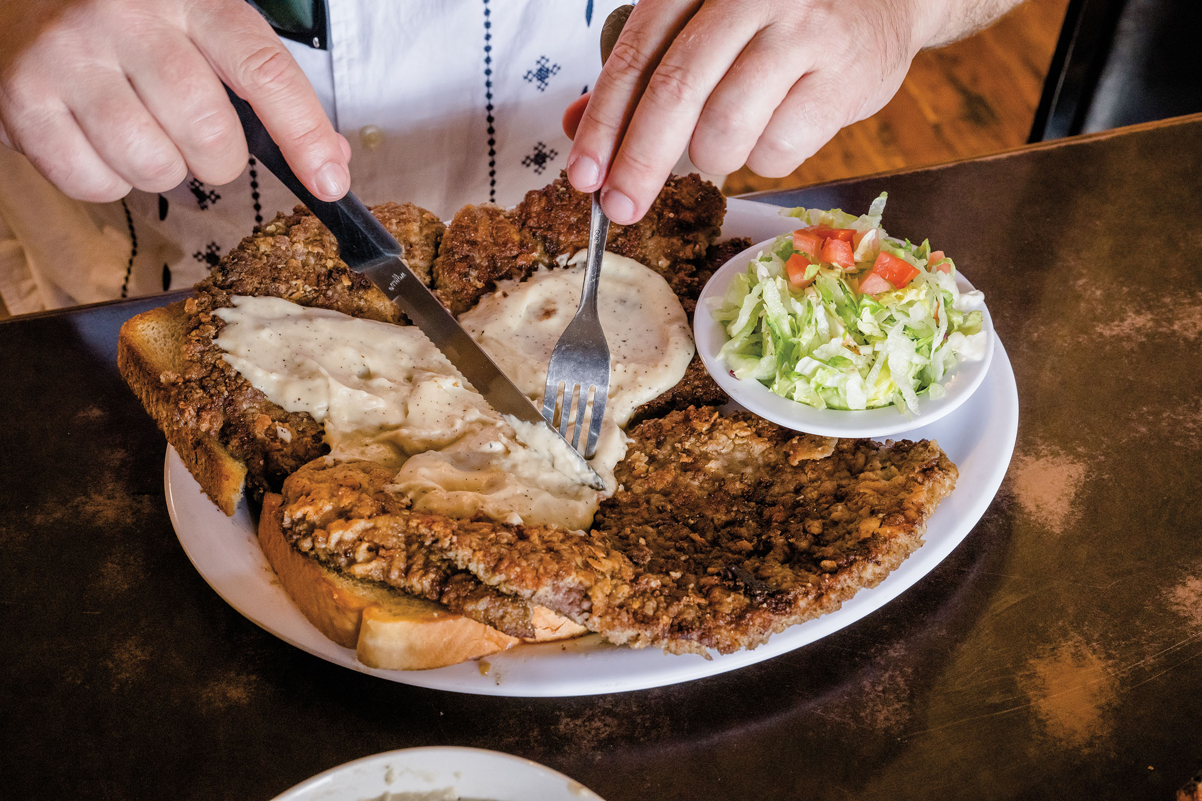 A knife and fork cut into a beautifully golden brown meal on toast with a side salad