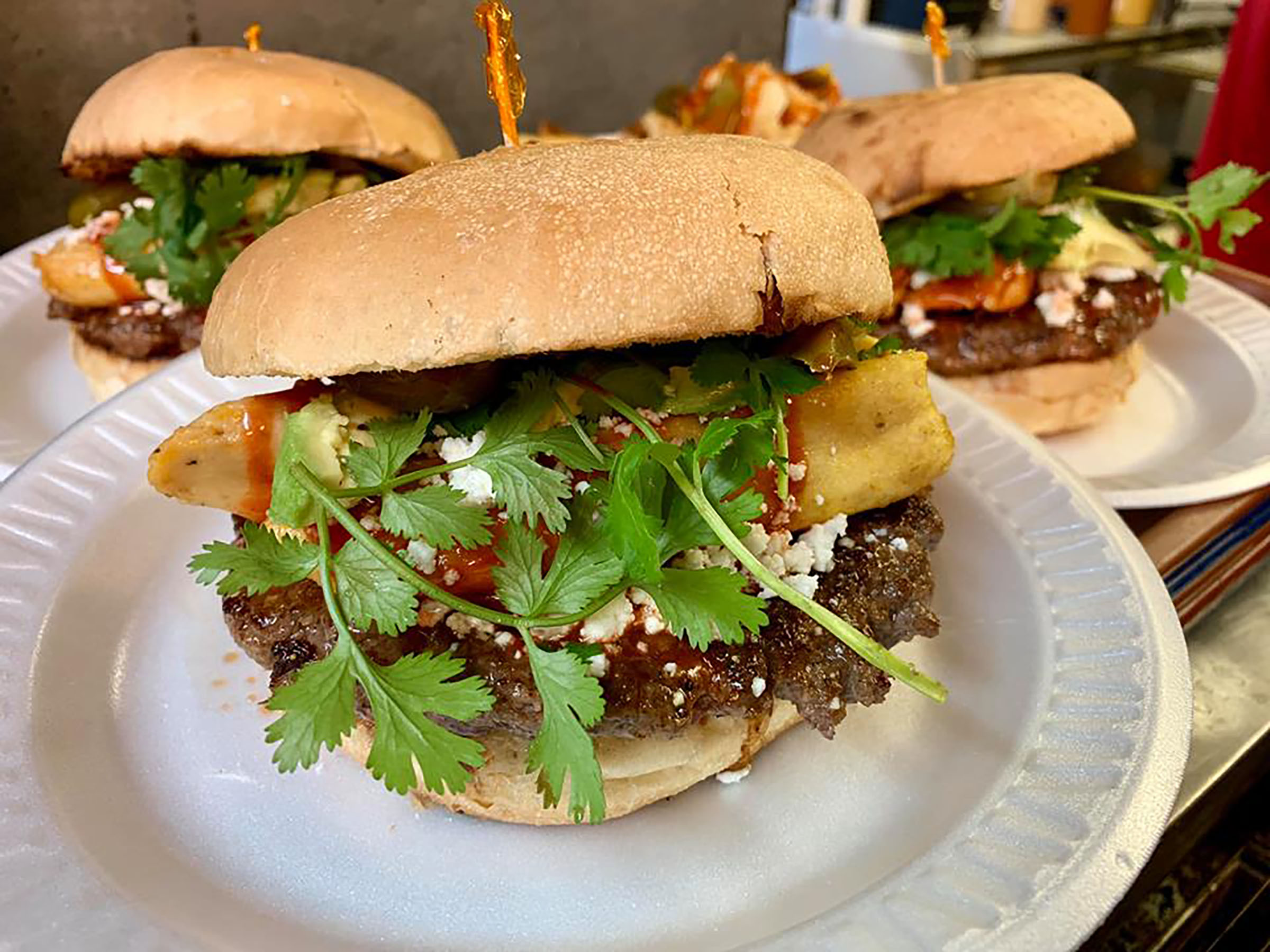 A cheeseburger topped with a tamale and cilantro