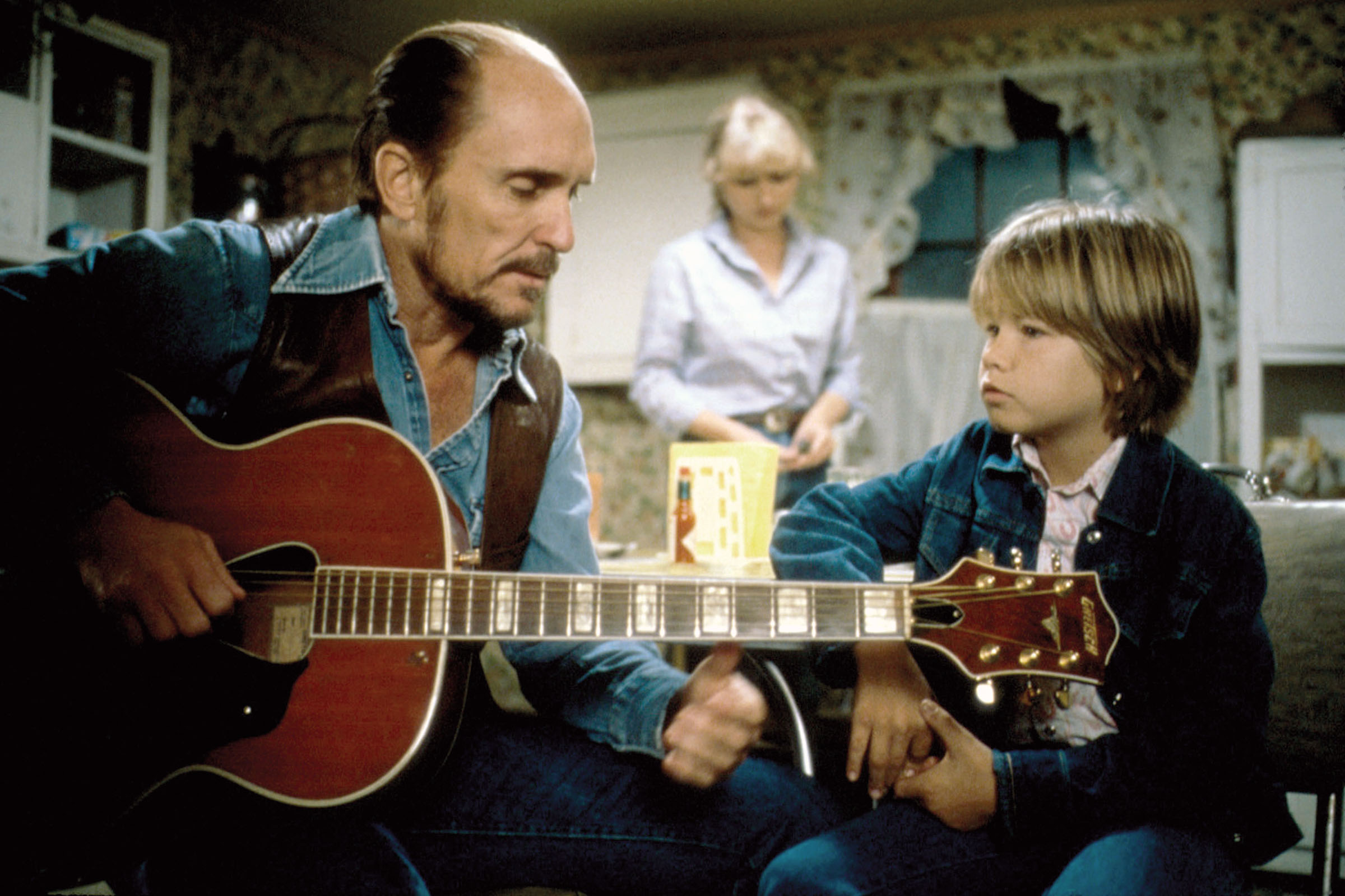 A movie still of an older man teaching a child to play guitar