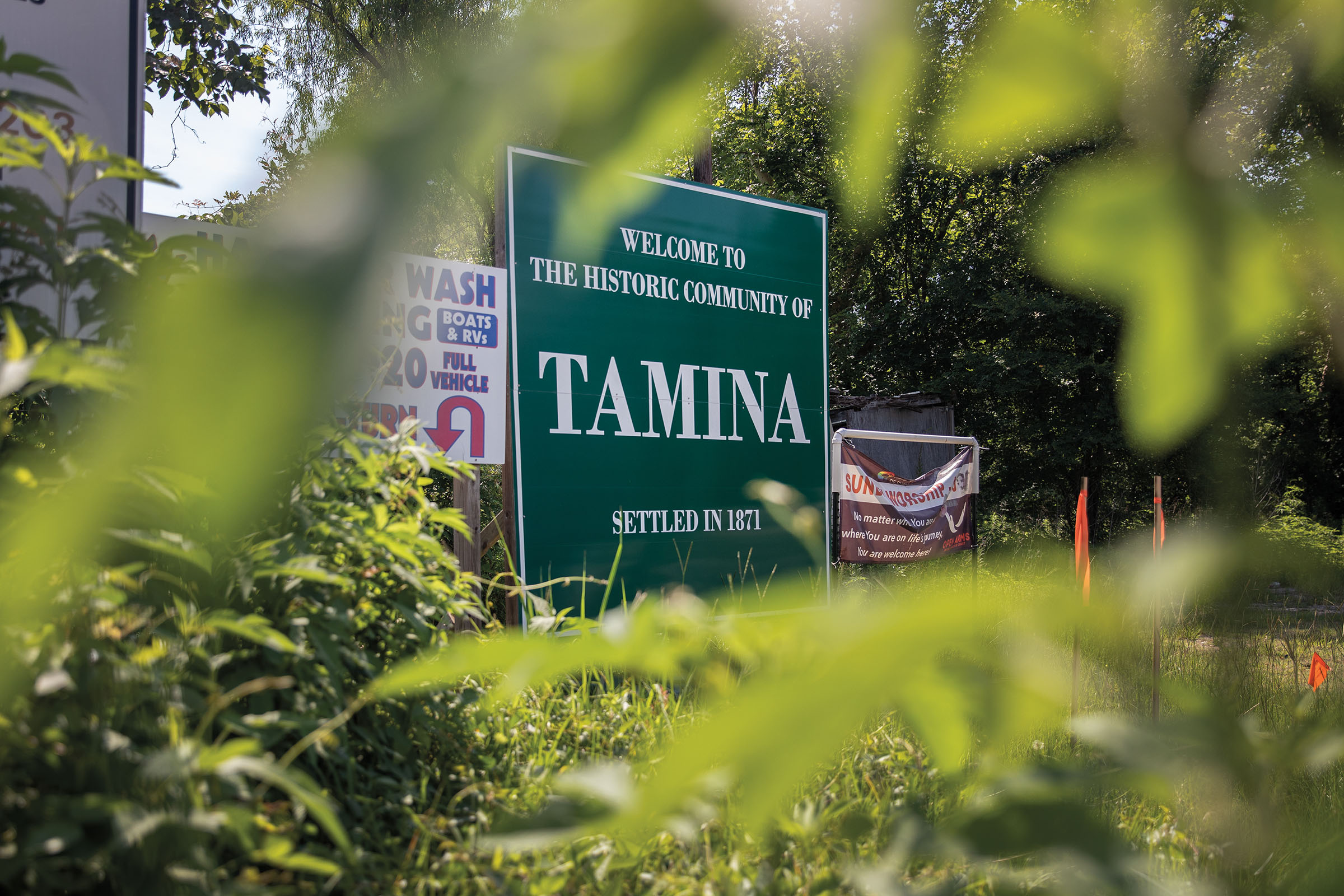 A large green sign reads "Welcome to the historic community of Tamina, settled in 1871"