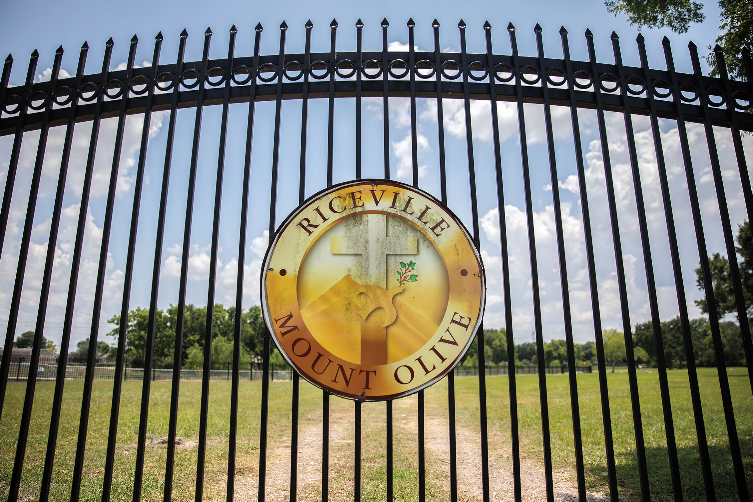 A golden circular sign sits outside of a black-gated cemetery