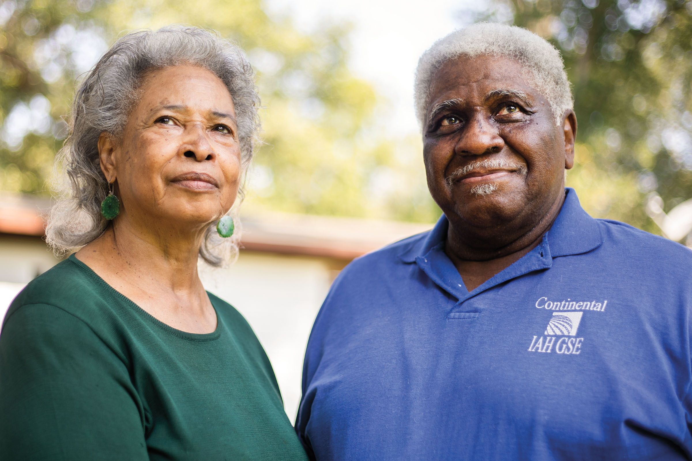 Two people look off into the distance in front of a soft outdoor background