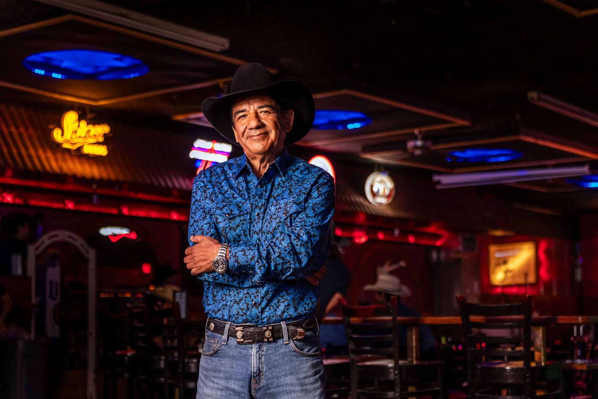 A man in a black and blue button down shirt smiles at the camera.