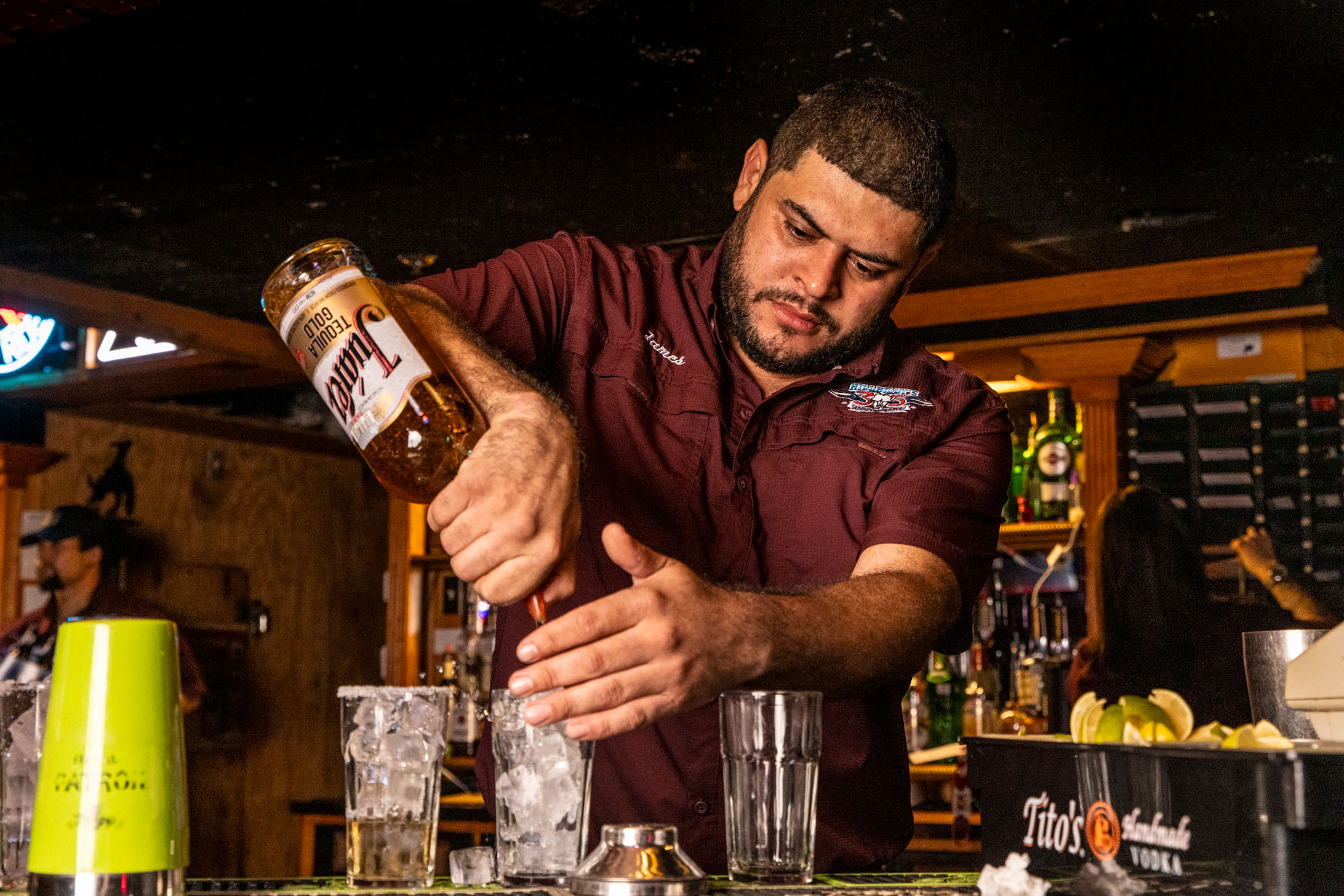 A man in a maroon shirt pouring an alcoholic beverage.