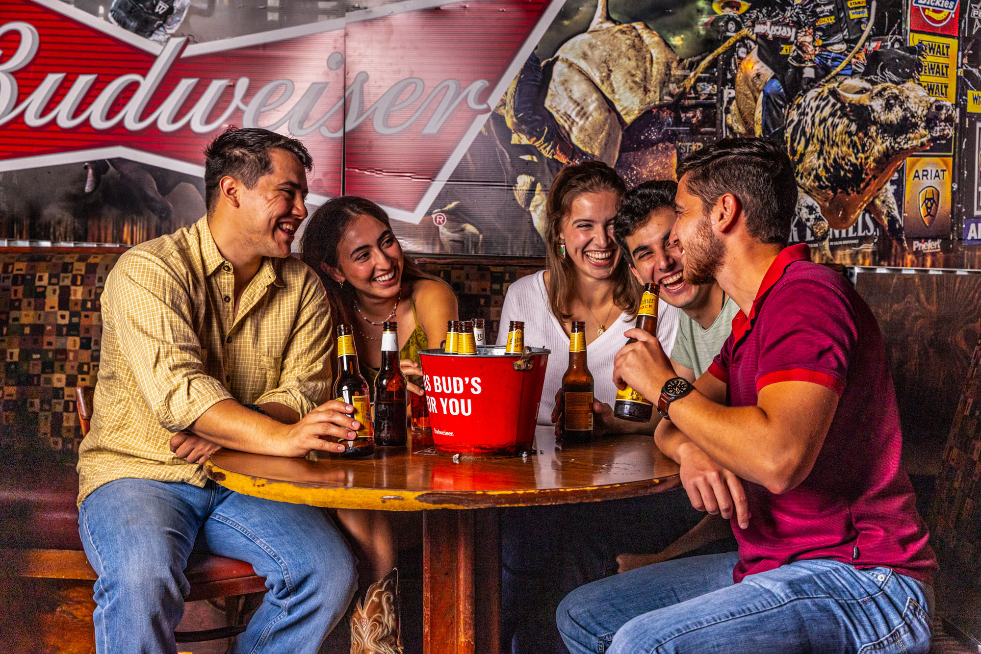 Five younger adults sitting at a table laughing while drinking.