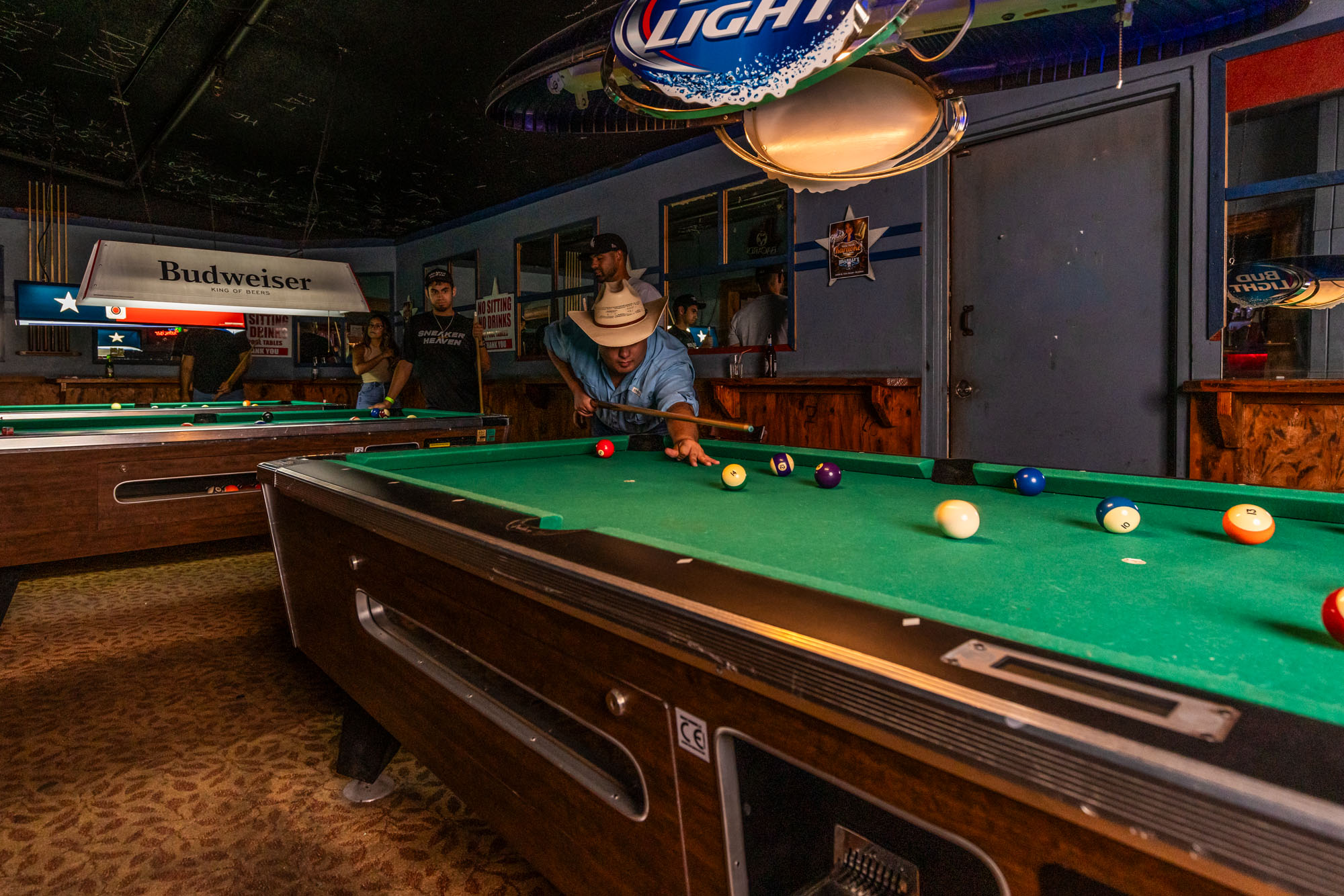 A man in a blue shirt and cowboy hat gets ready to hit a billiard ball.