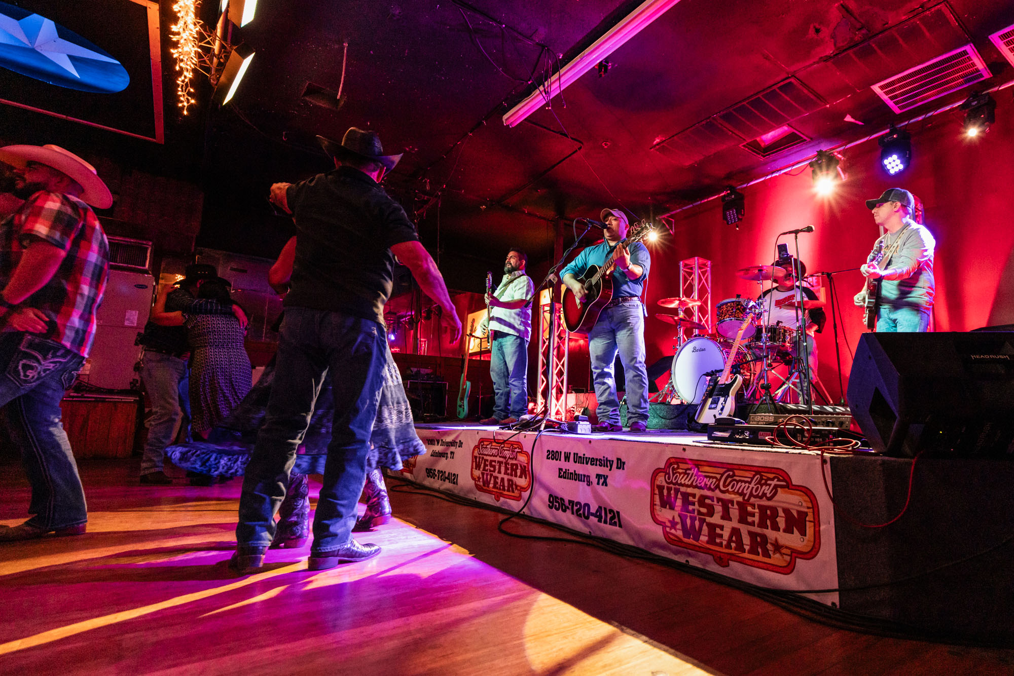 A band performs on a stage under pink and purple lights