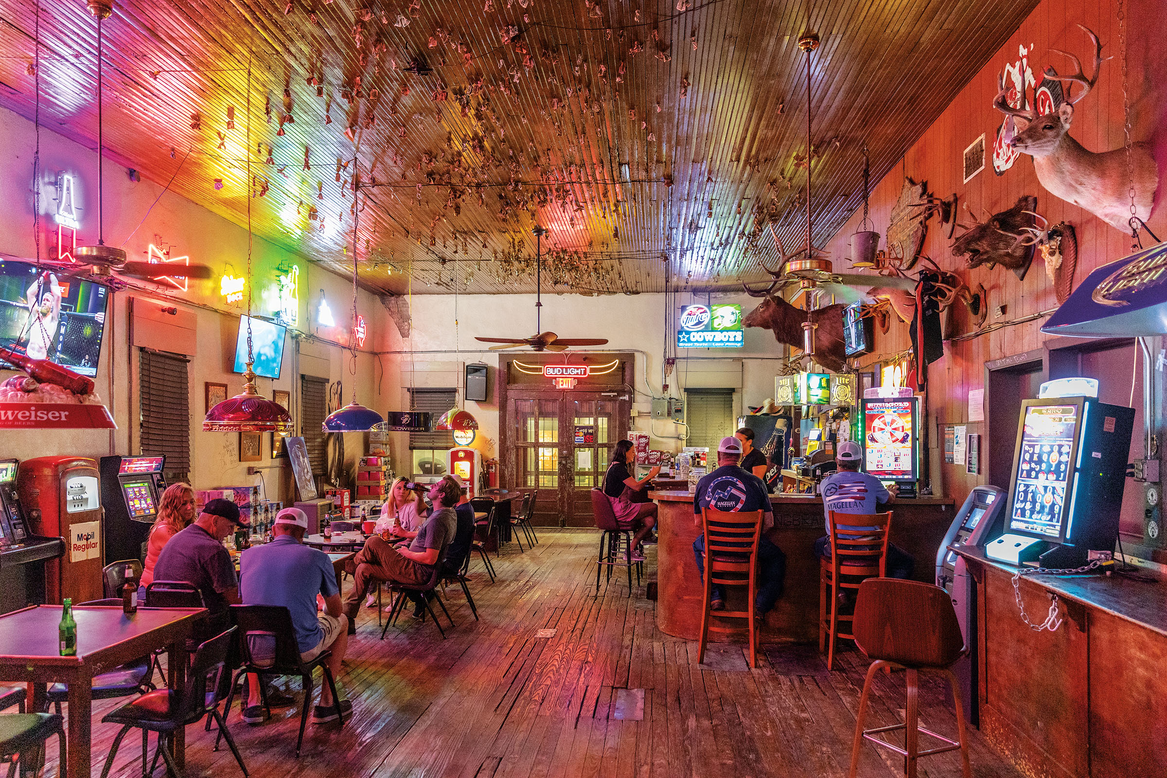 Patrons sit at a brightly-colored bar with wooden ceiling and dollar bills