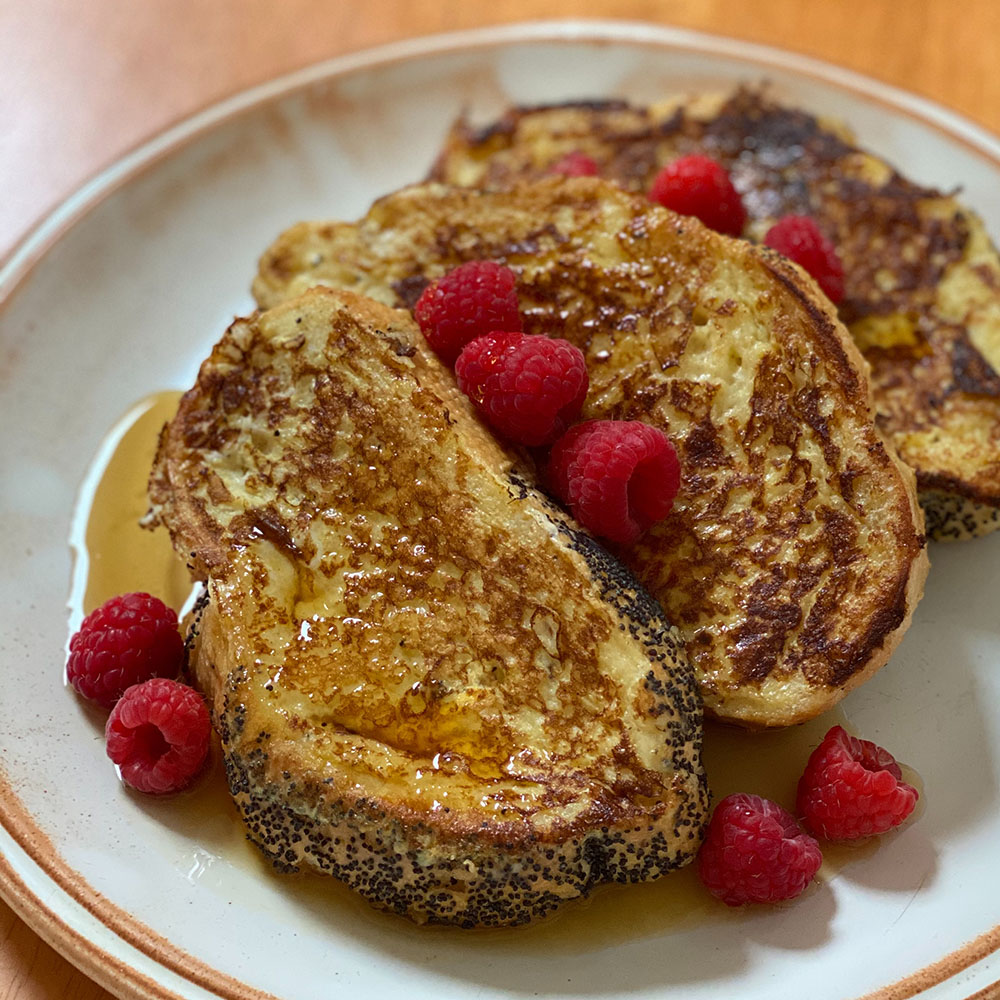 A photograph of thick slices of golden brown french toast with raspberries on top