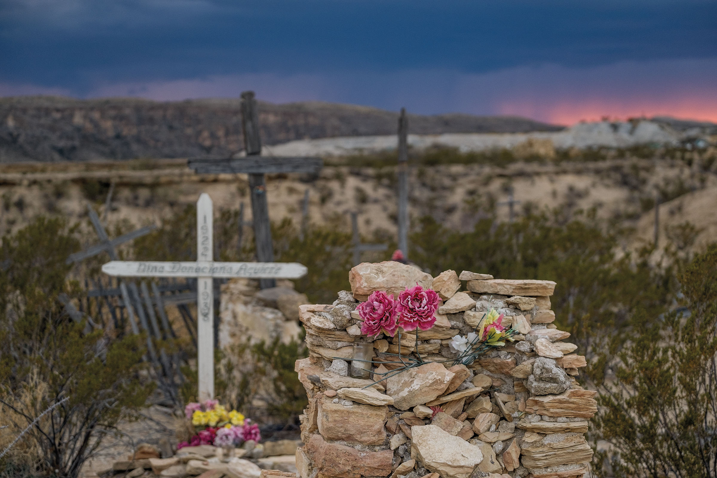 A gravesite with a white cross and flowers on rocks