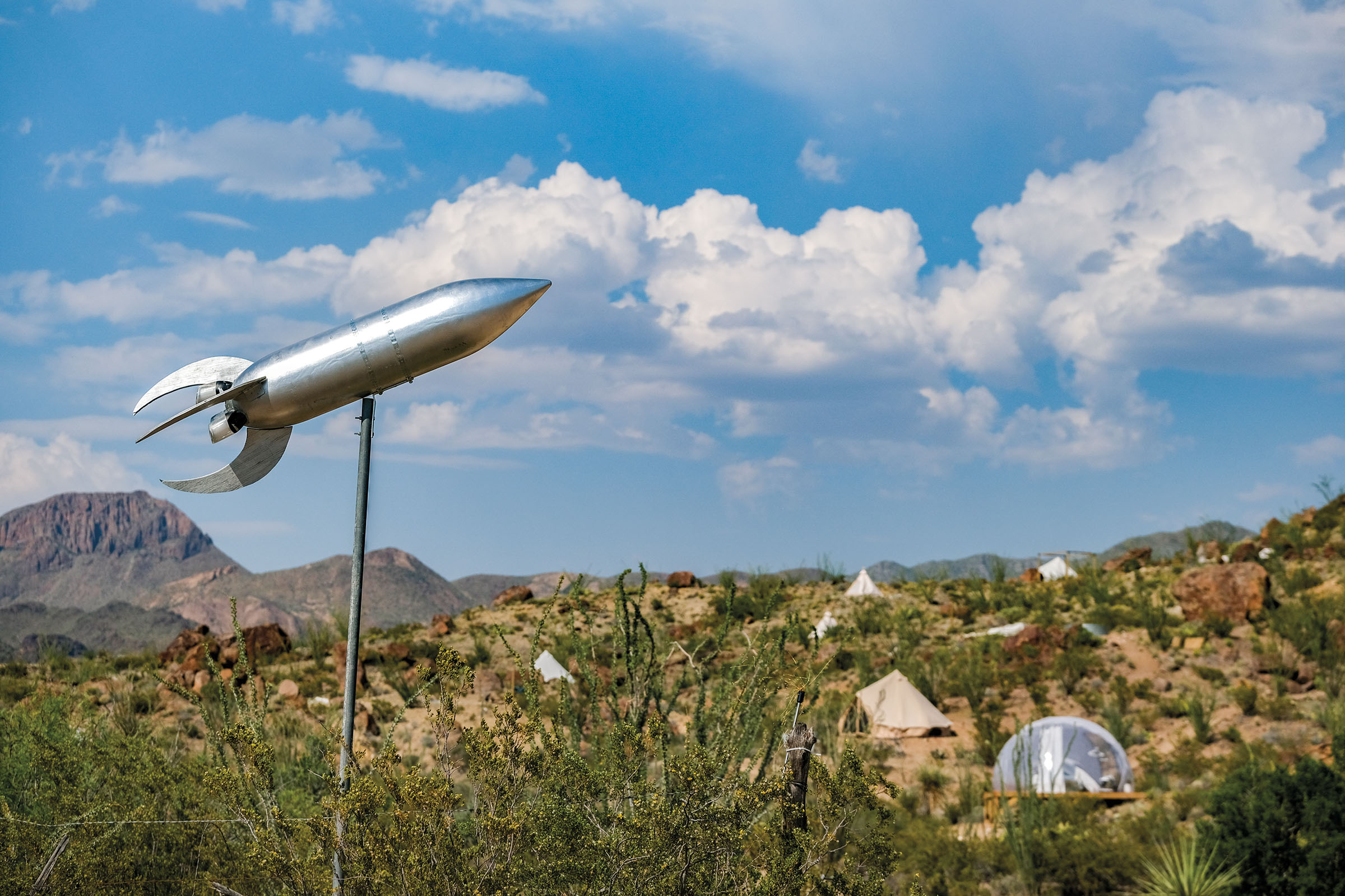 A silver rocket in front of a desert landscape with clouds and blue sky