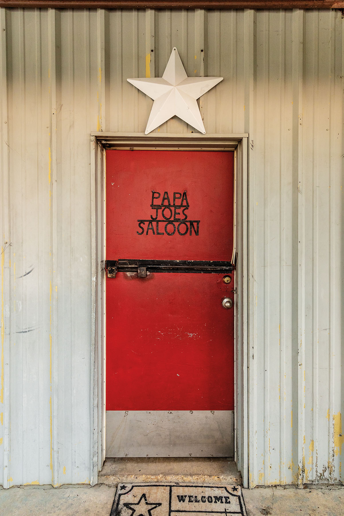 The exterior of a metal building with a red door reading "Papa Joe's Saloon"
