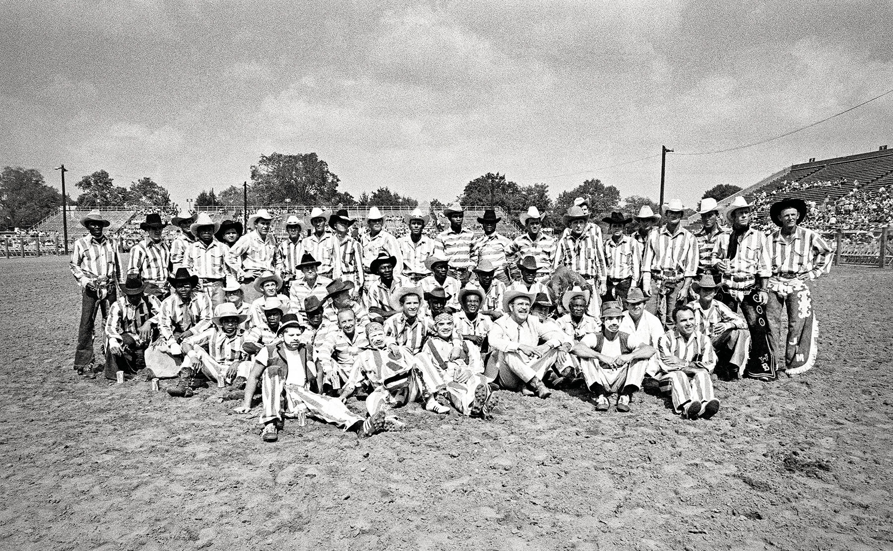 A large group photo of people sitting on the dirt ground