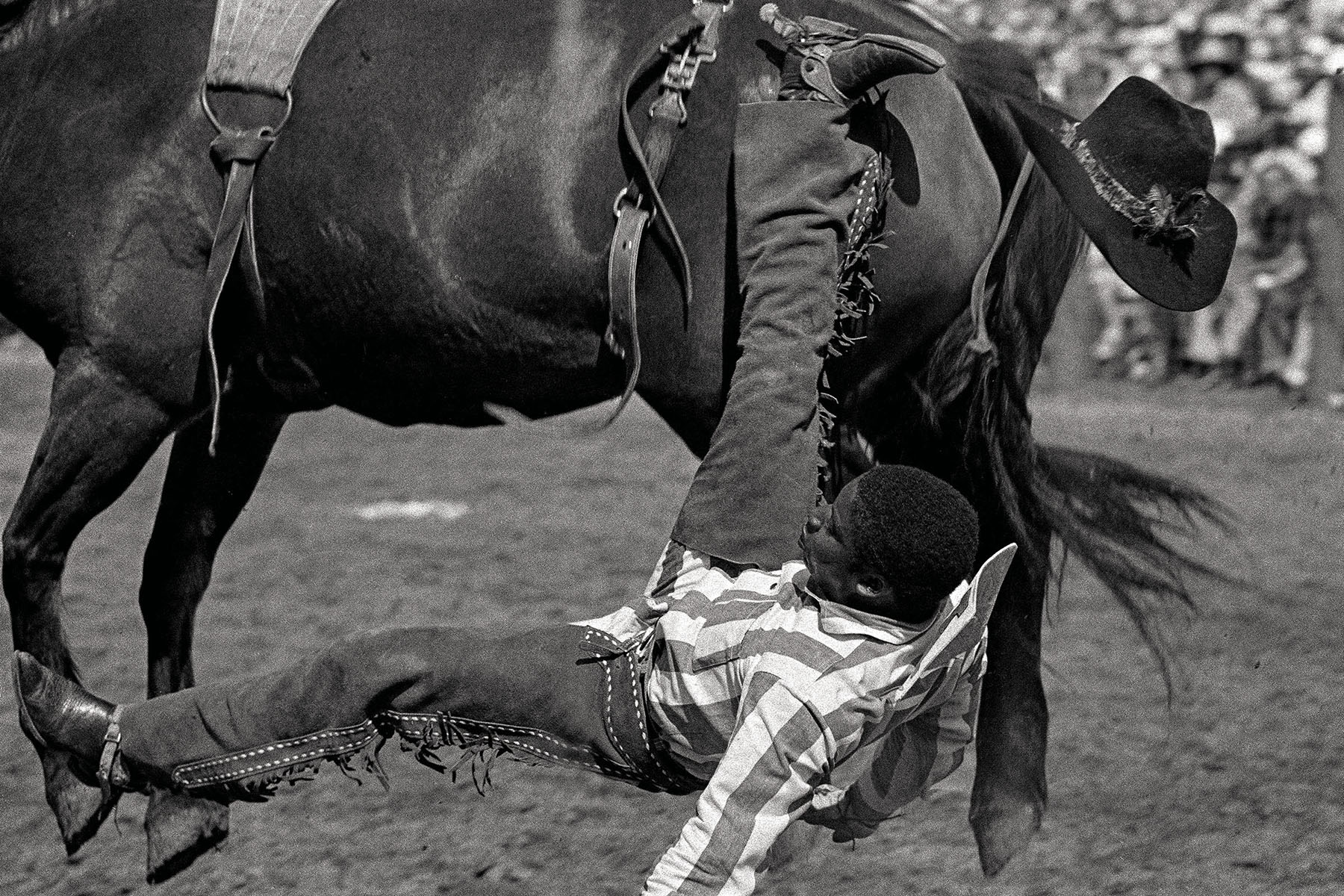 A man falls off the side of a horse onto dirt ground