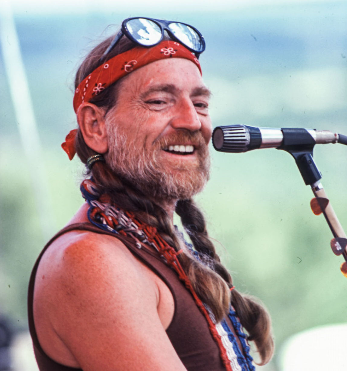 An older man smiling near a microphone while performing.
