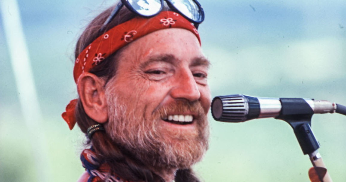 An older man with a beard and bandana smiling close to a microphone.