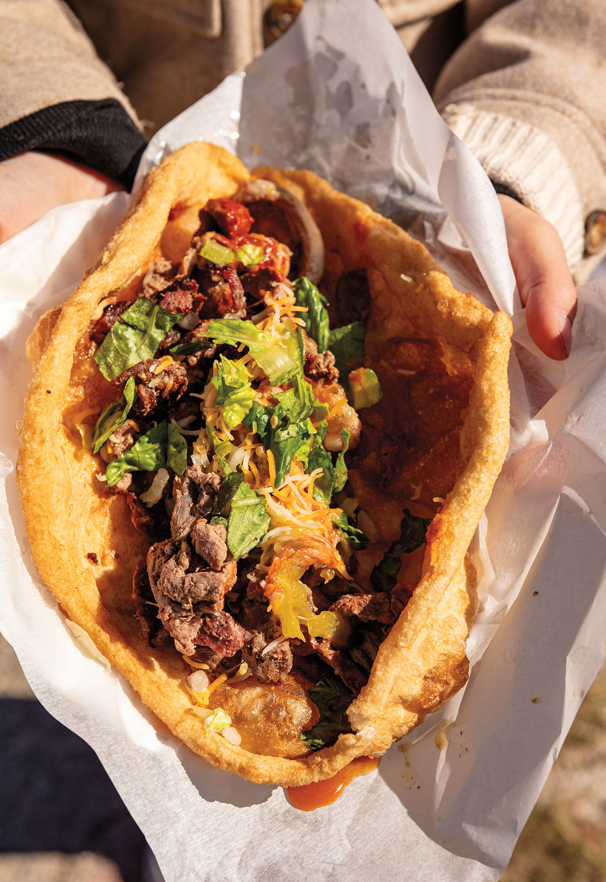 An overhead view of meat, beans, cheese, spices, and vegetables contained in fry bread