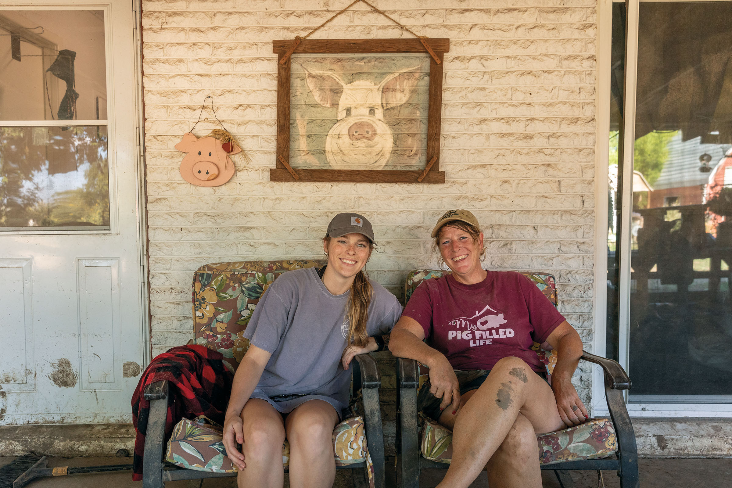 Two people sit on an outdoor couch underneath a framed art print of a pig