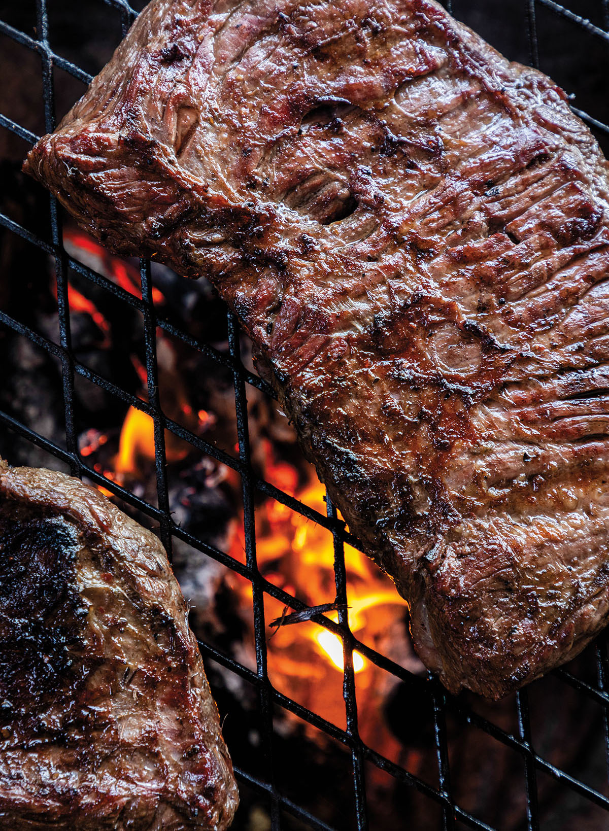 An overhead view of fajita meat cooking over fire on a grill