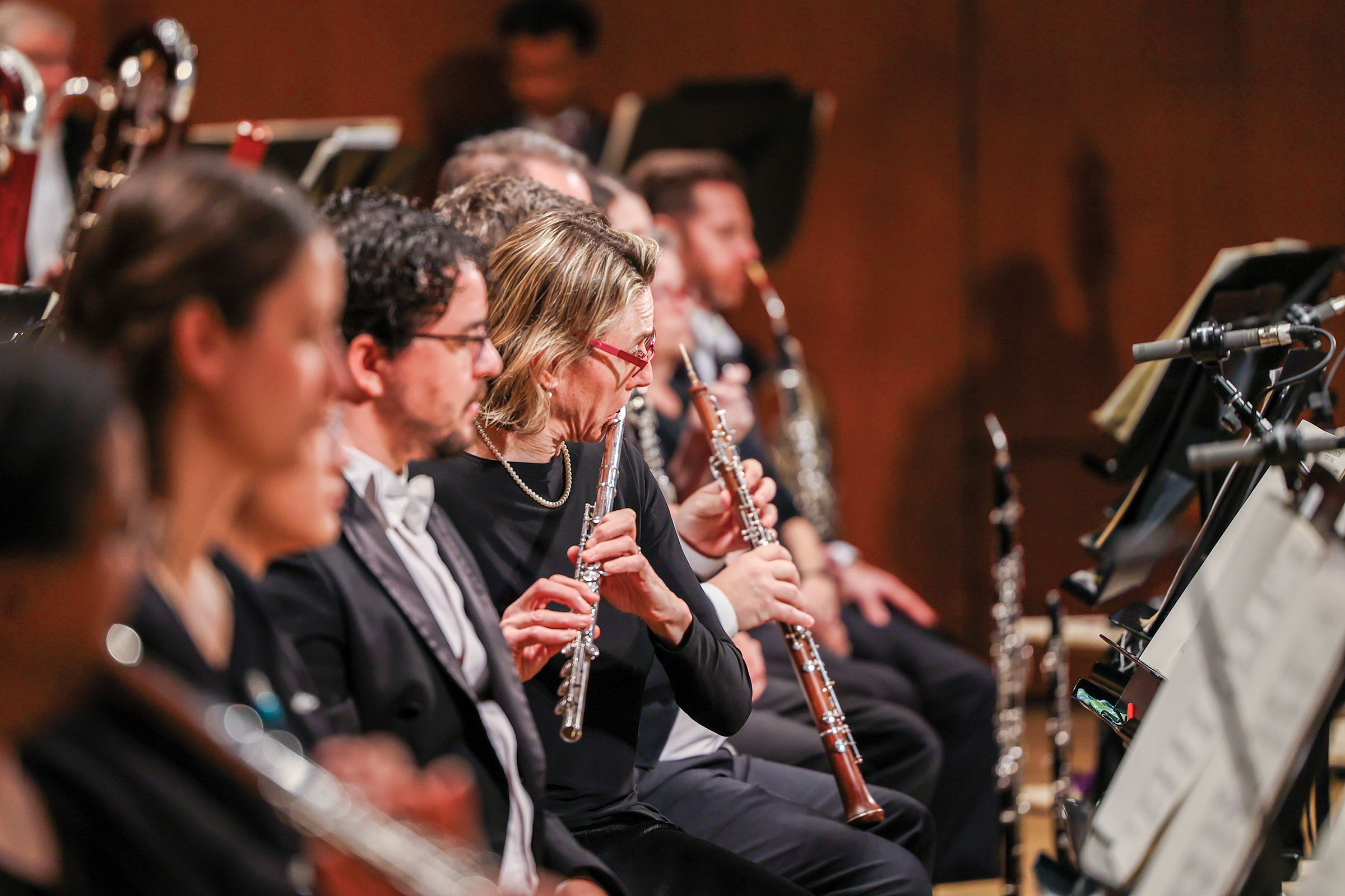 A group of performers play woodwind instruments like clarinet, bassoon, and flute