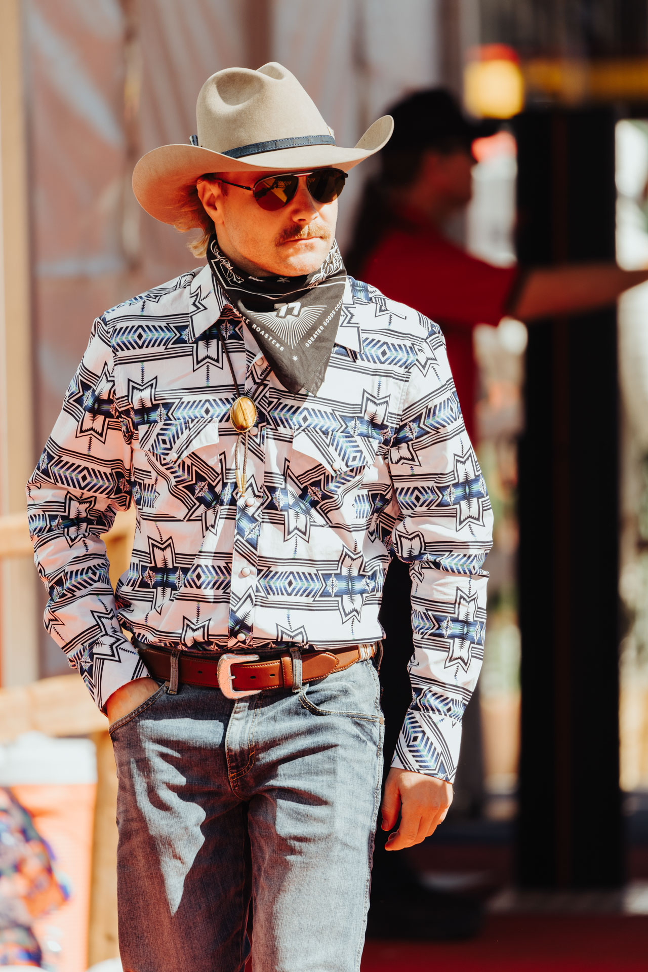 A man in a cowboy hat and bandana poses for the camera wearing Aviator sunglasses