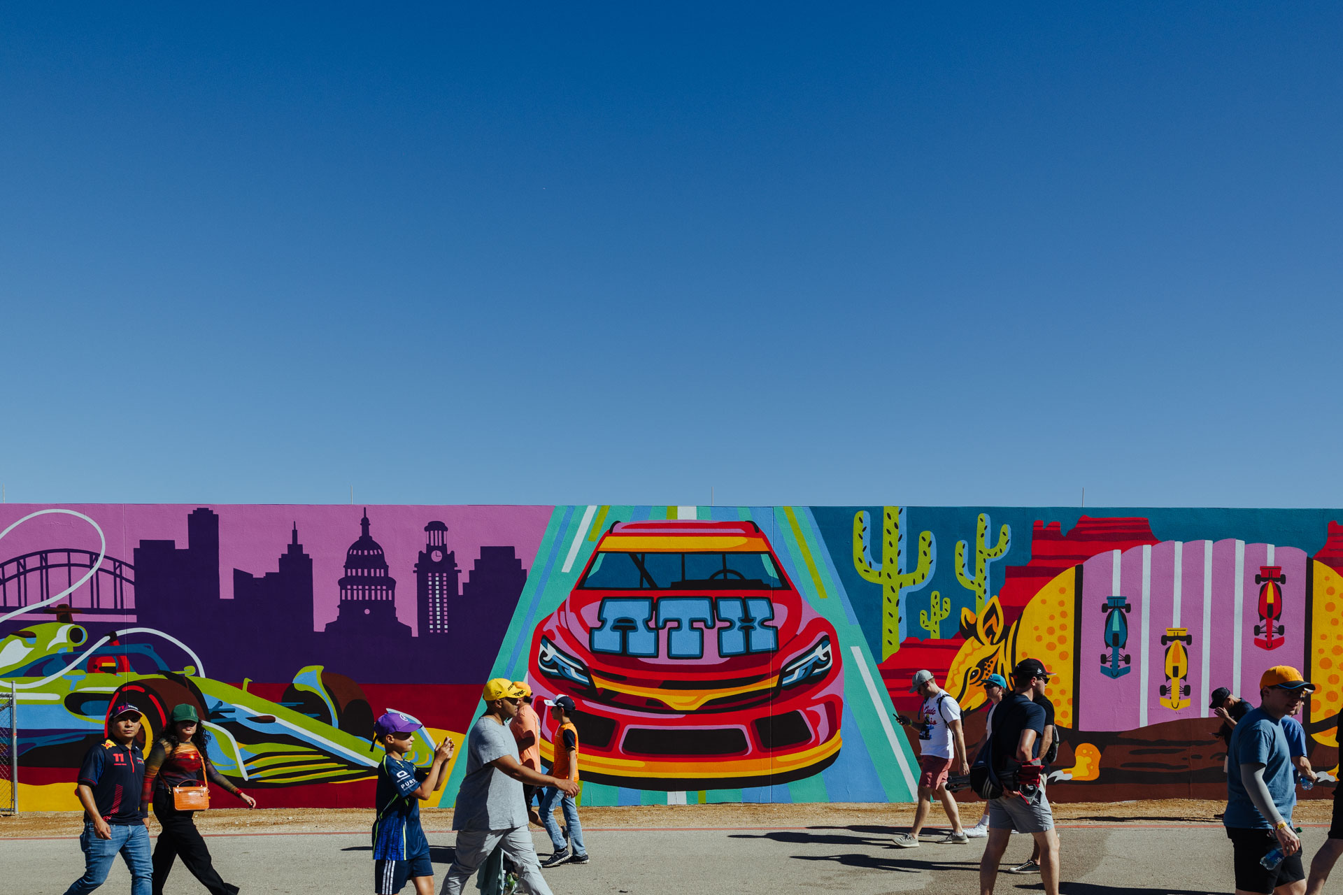 A group of people walk in front of a colorful mural with a racecar labeled with ATX