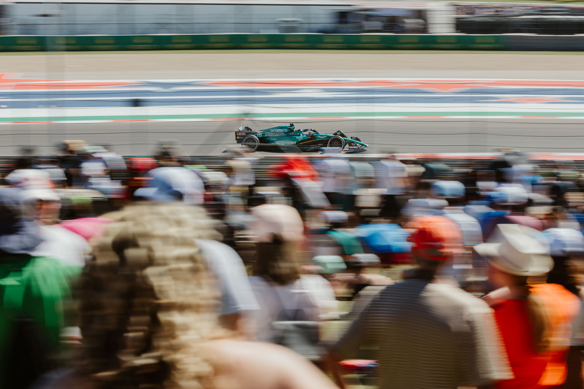 The blur of a green racecar is visible in front of a crowd of people