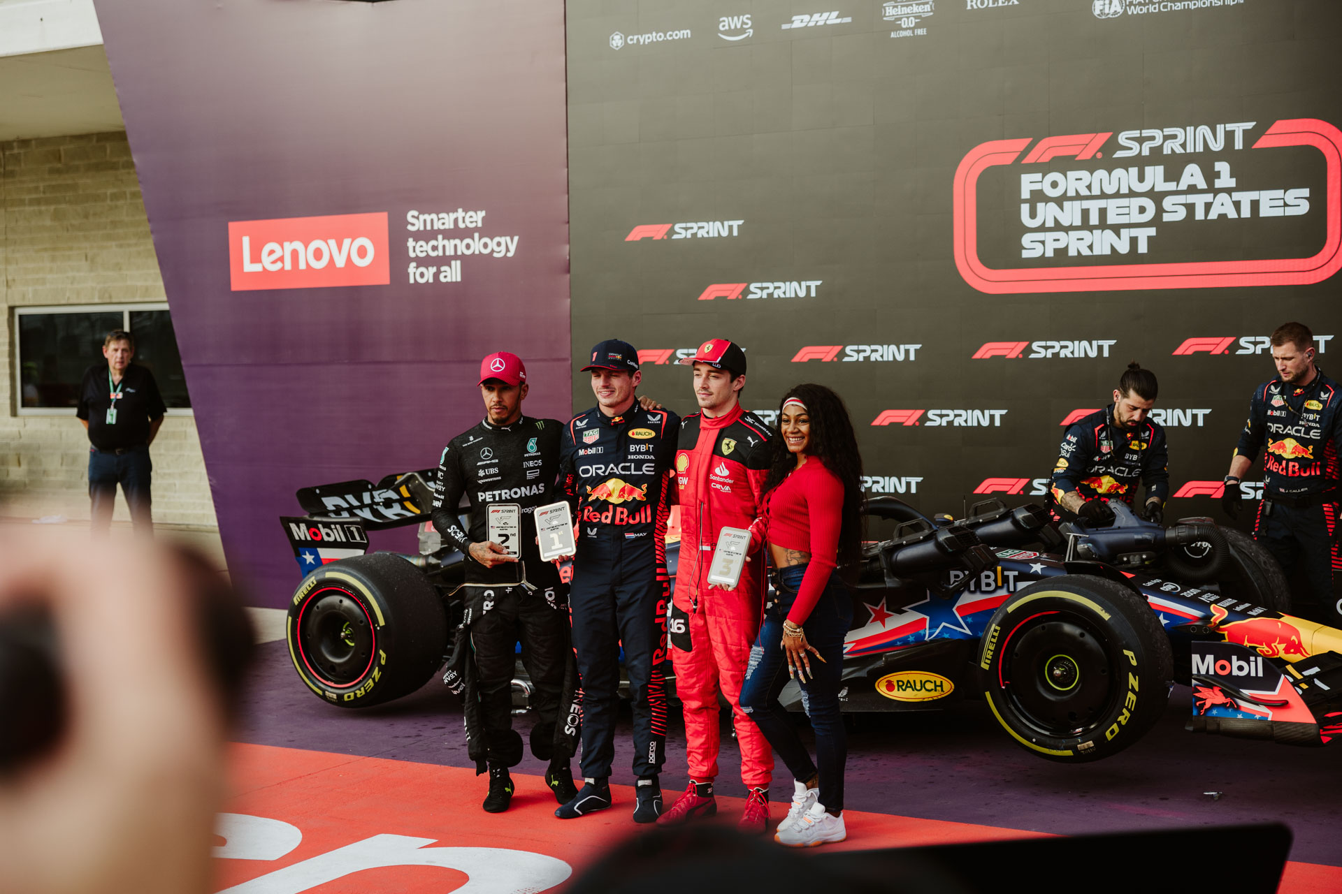 A group of four people, three in Red Bull Racing uniforms, pose in front of an F1 car