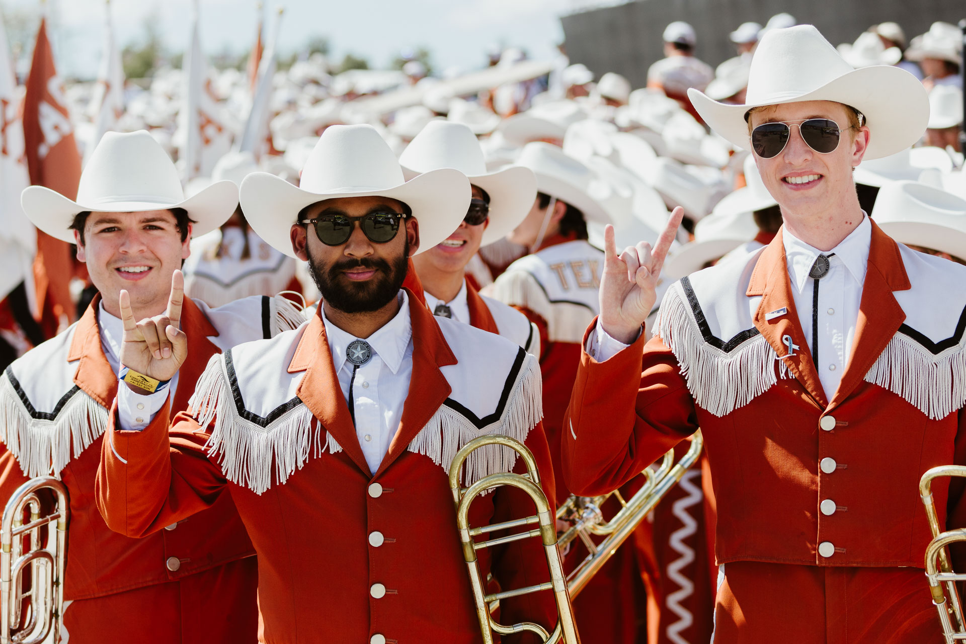 A small group of members of the Longhorn Band flash the 'Hook em Horns' hand sign wearing marching band attire