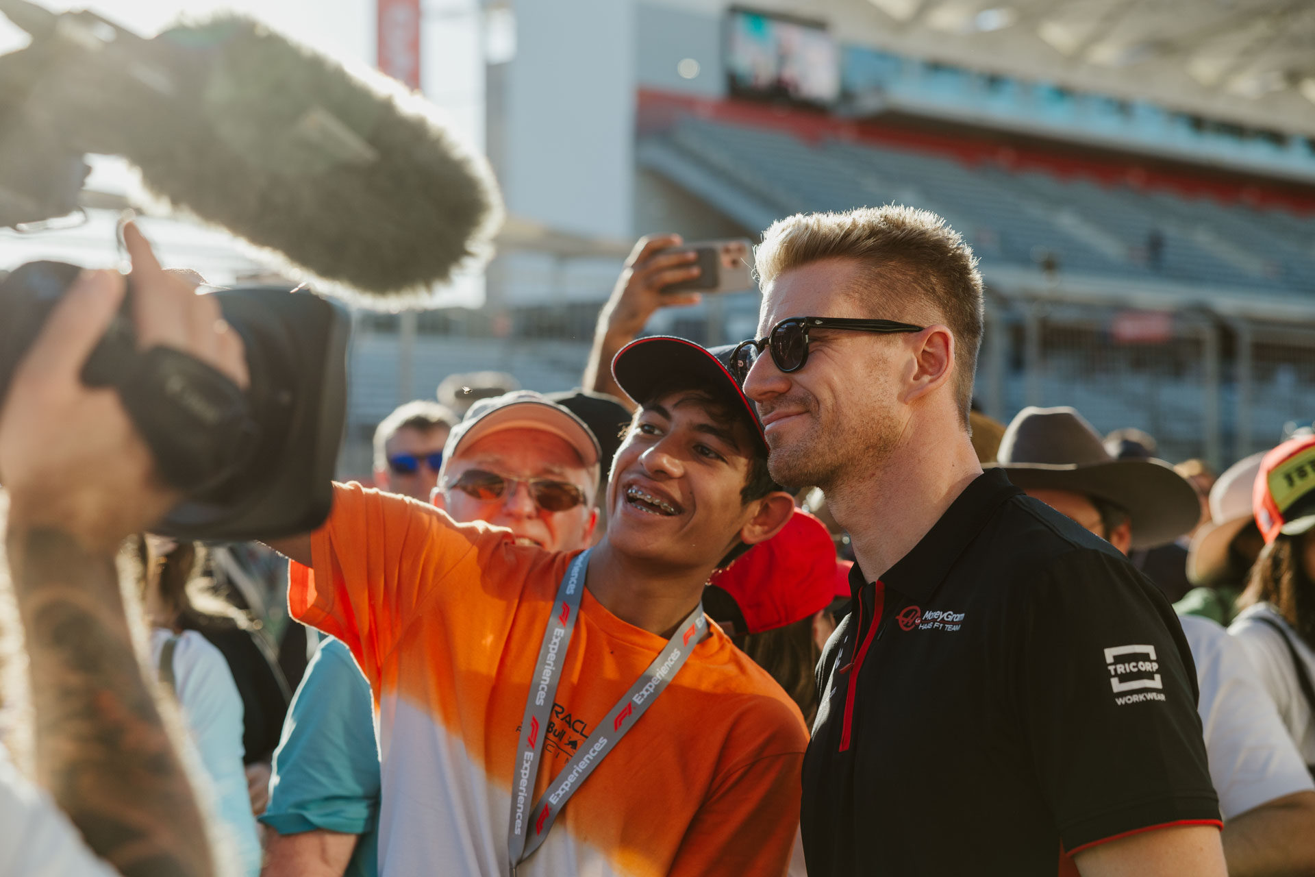 A fan dressed in orange poses with a driver wearing black and sunglasses