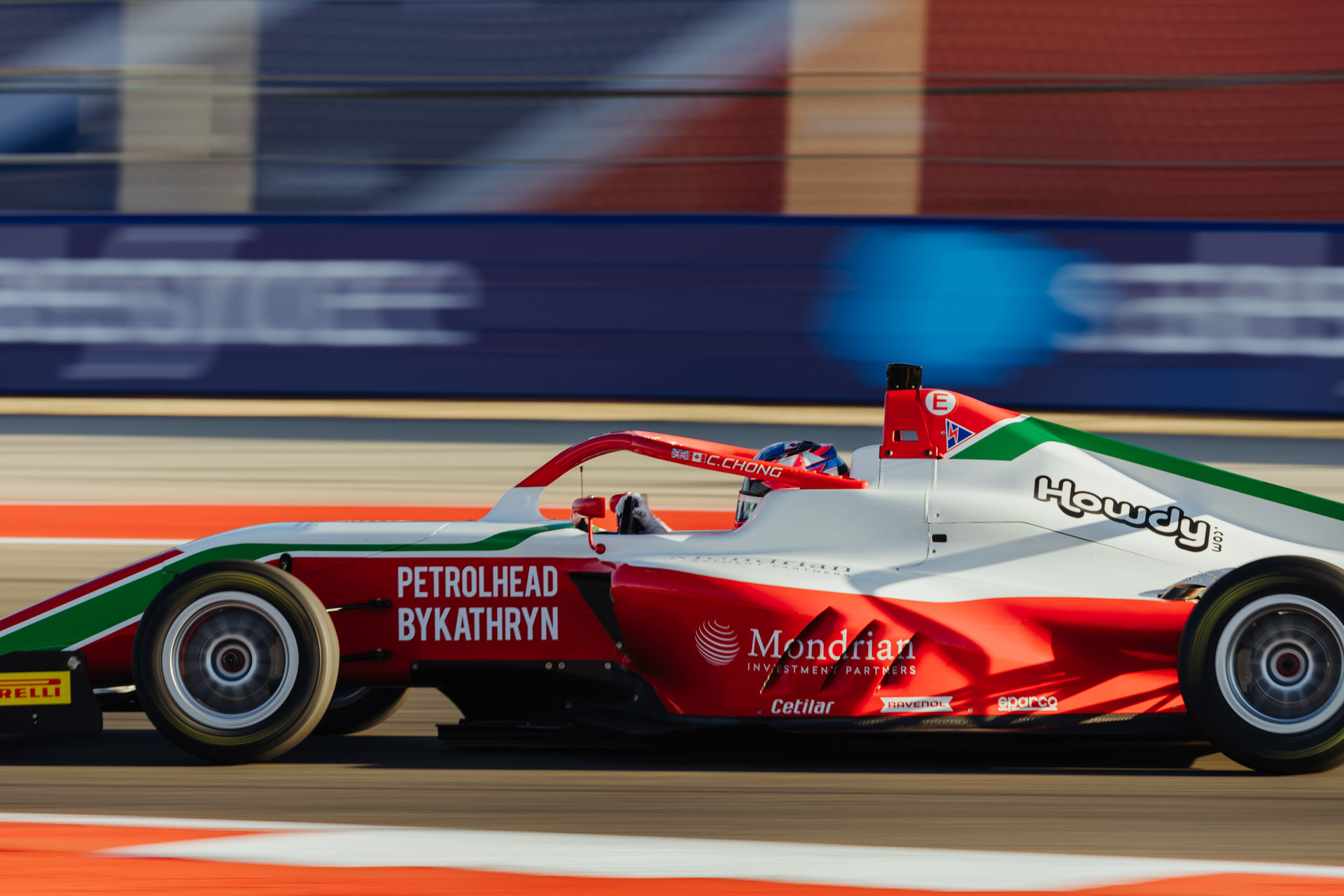 A red, white, and green car labeled with the words 'Petrolhed by Kathryn' drives past a crowd of people
