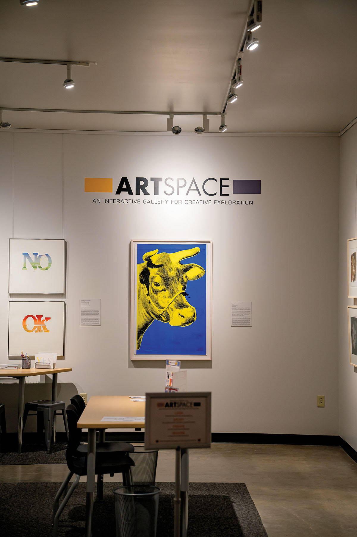 The inside of a museum, focused on a wall reading "Art Space" and a picture of a cow on a blue background