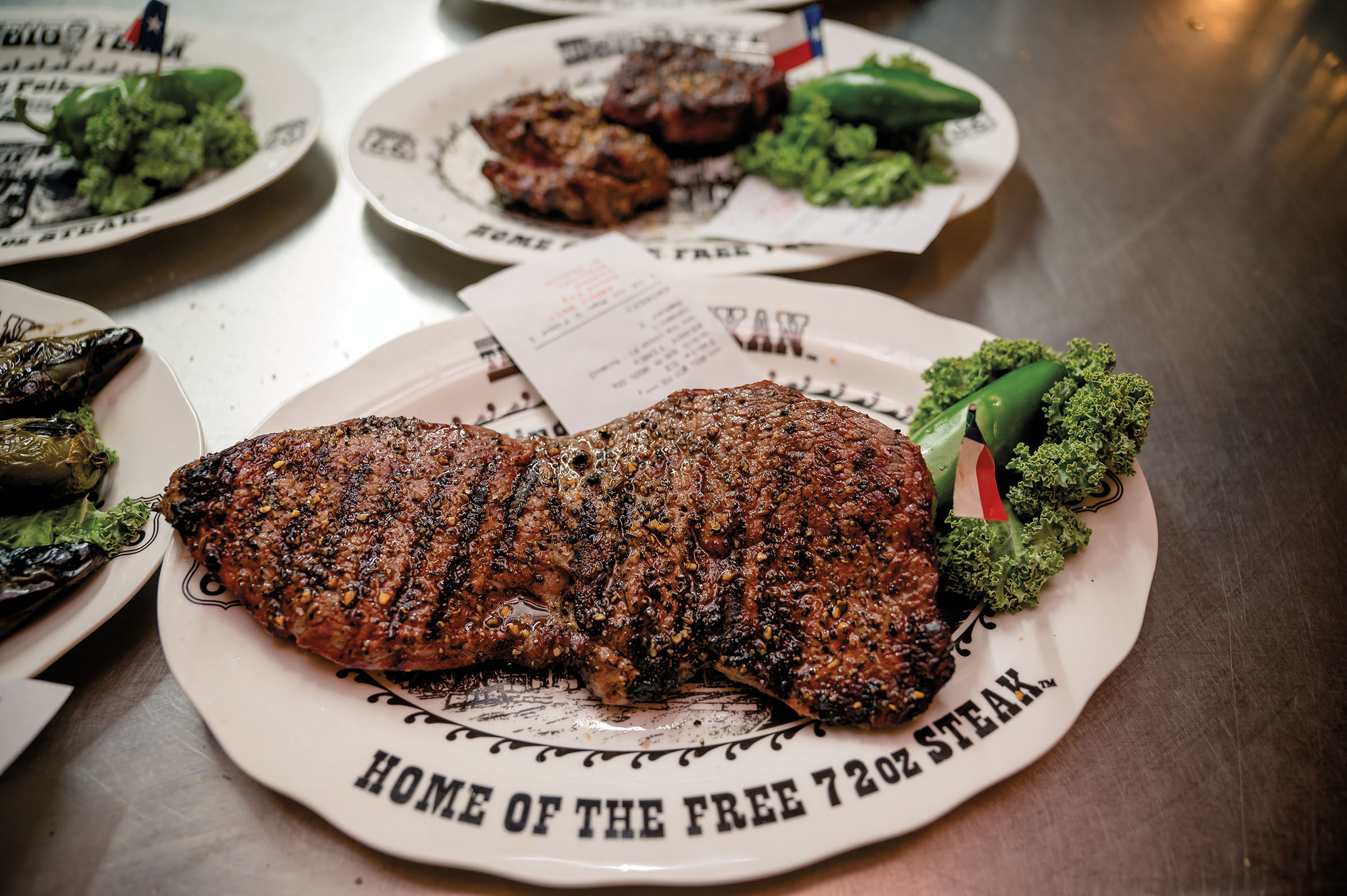 A large steak with grill marks and a few pieces of broccoli sits on a white plate reading "Home of the free 72oz steak"