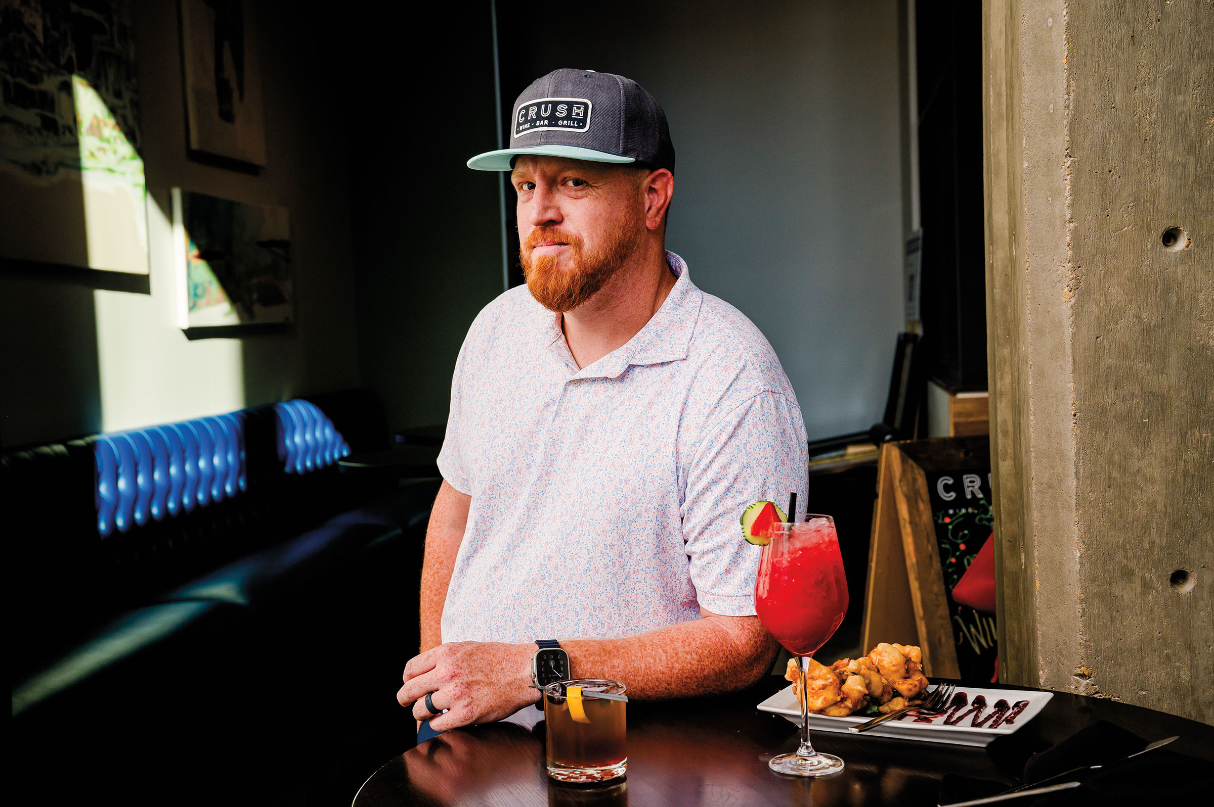 A man in a gray baseball cap stands leaning on a bar