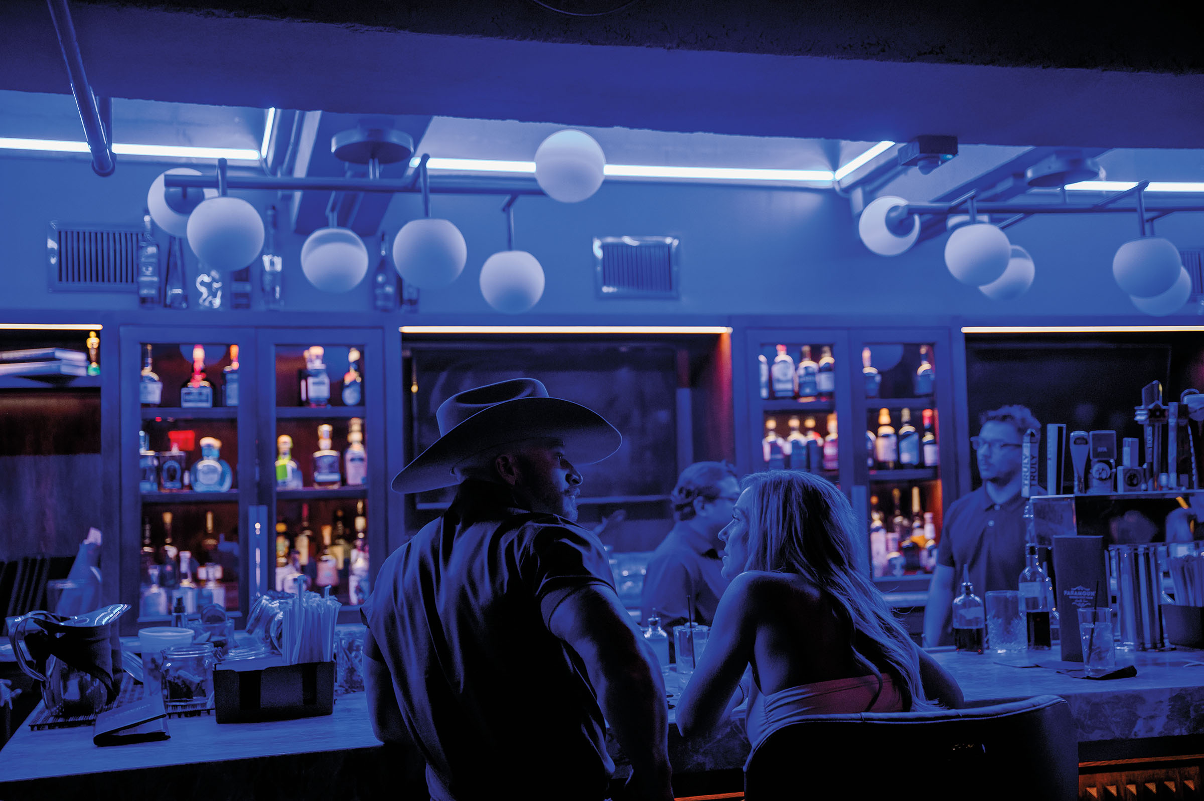 People sit around a dimly-lit bar with large circular lamps