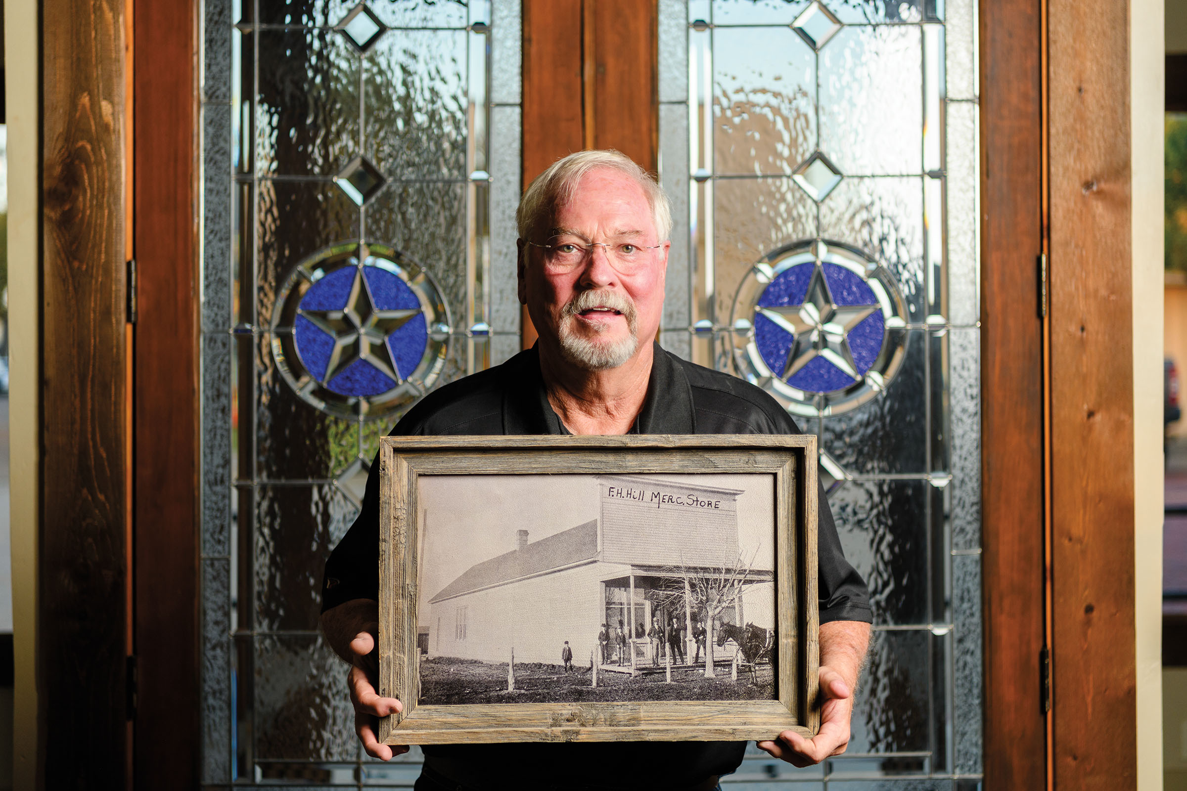 A man holds a vintage photograph in front of a stained-glass window