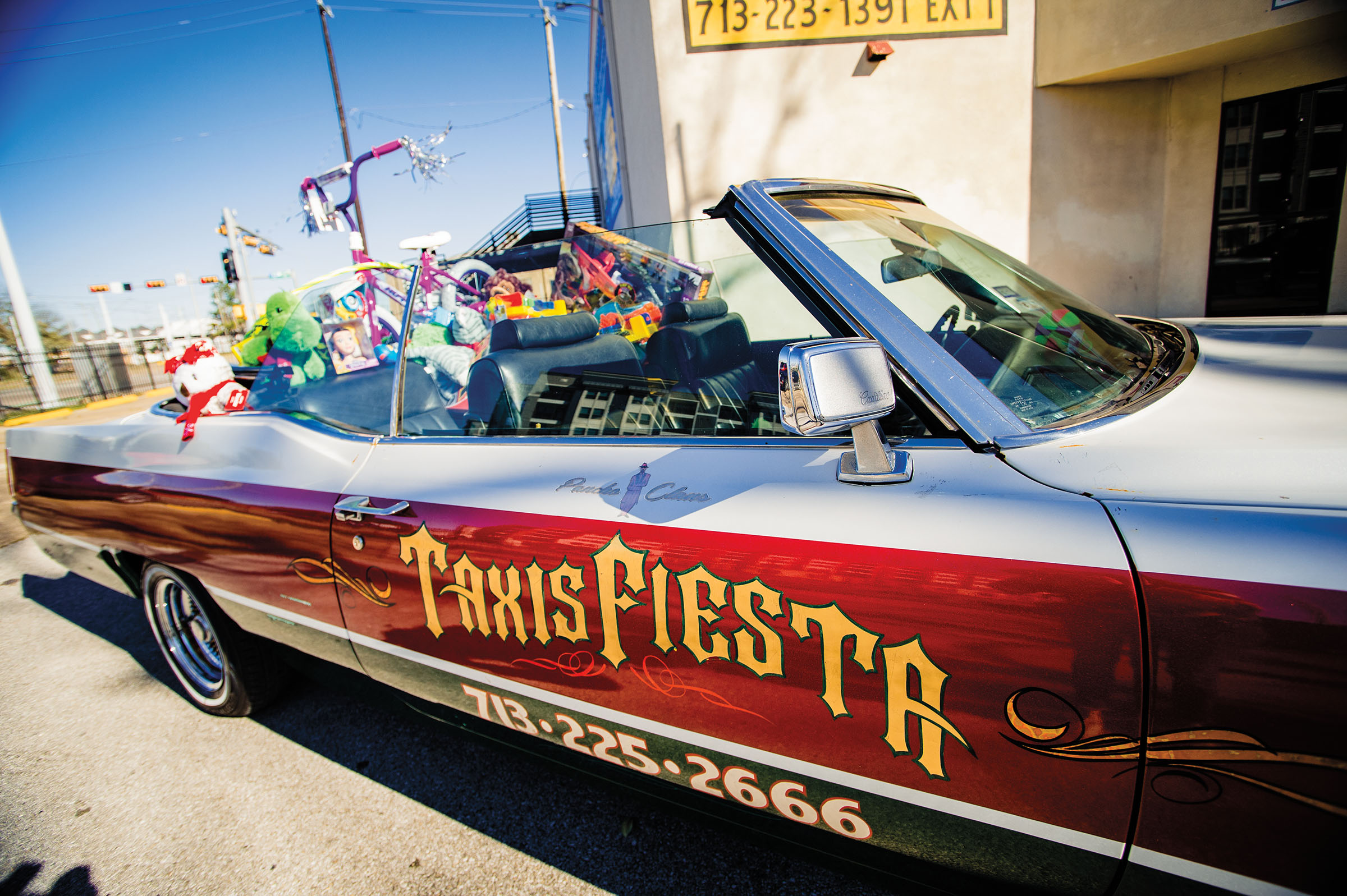 A long red and white convertible with "Texas Fiesta" on the side is filled with gifts on a sunny day
