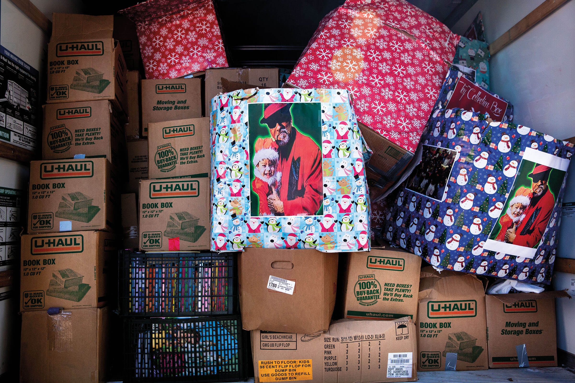 The back of a U-Haul trailer loaded with numerous cardboard boxes. Some are decorated with wrapping paper and pictures of Pancho Claus in his red zoot suit