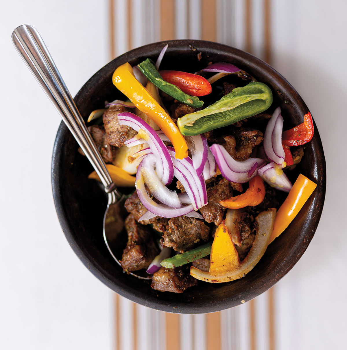 An overhead view of a bowl of vegetables on a striped placemat