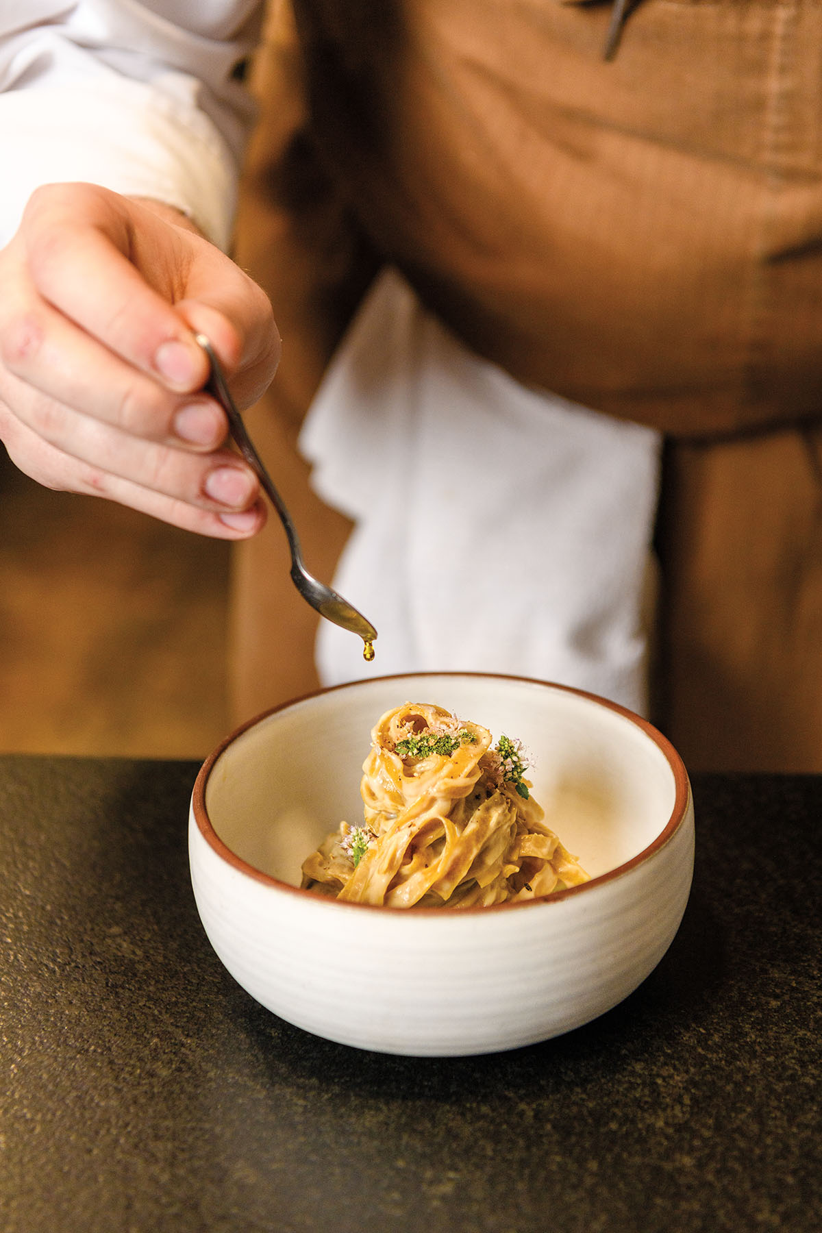 A person in a tan apron carefully plates long golden pasta noodles