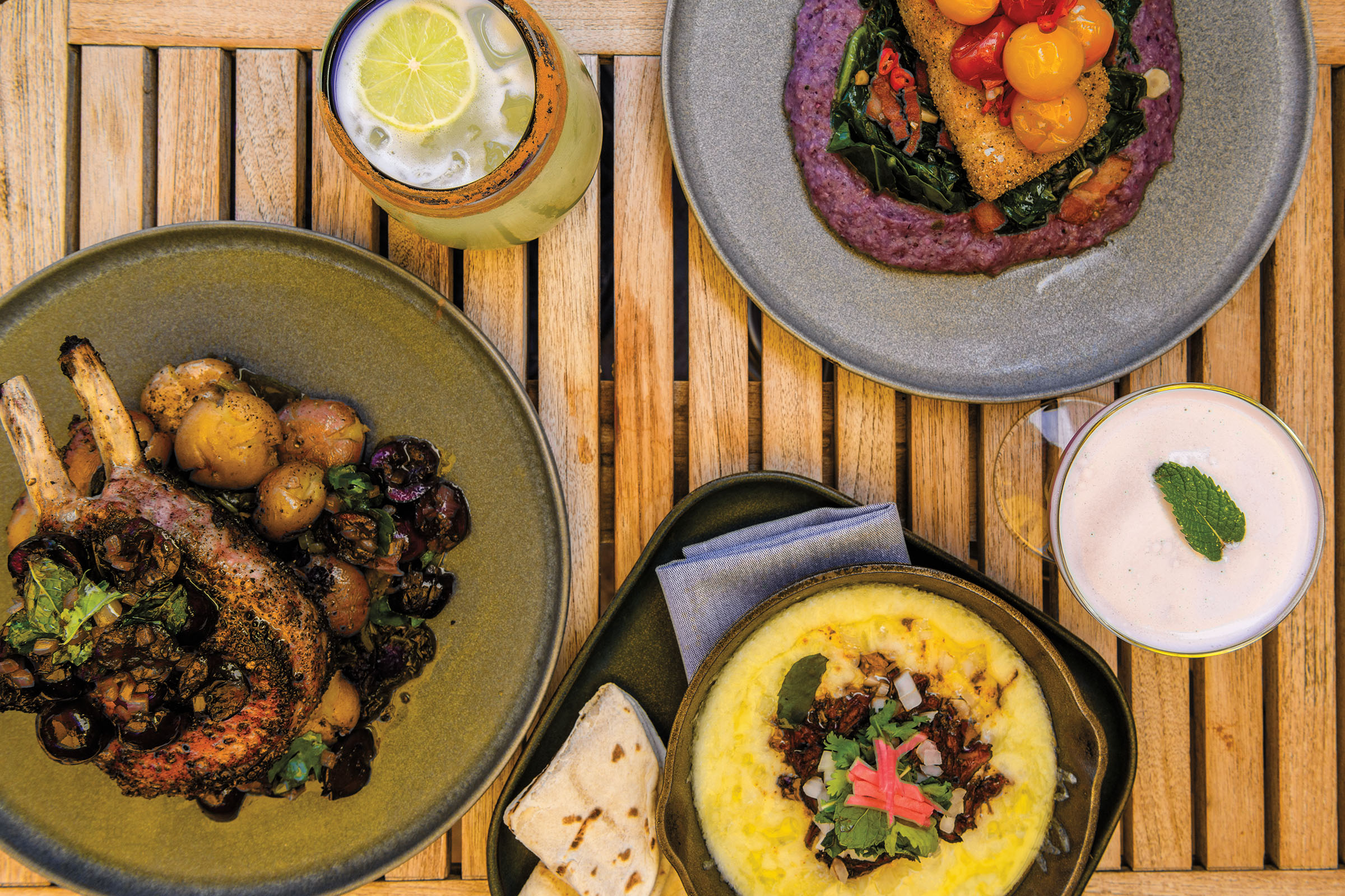 An overhead view of numerous colorful dishes on earth-toned plates and a wooden table