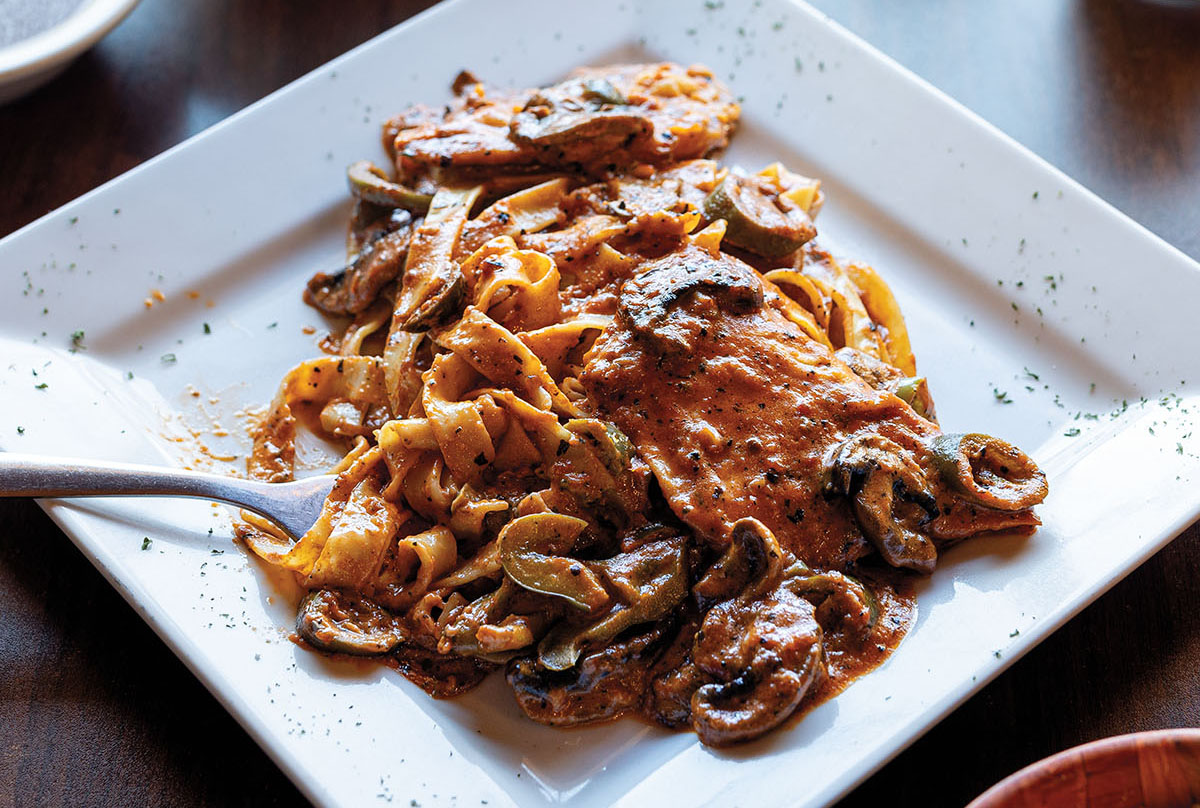 An overhead view of a plate of pasta in red sauce with mushrooms and wide noodles