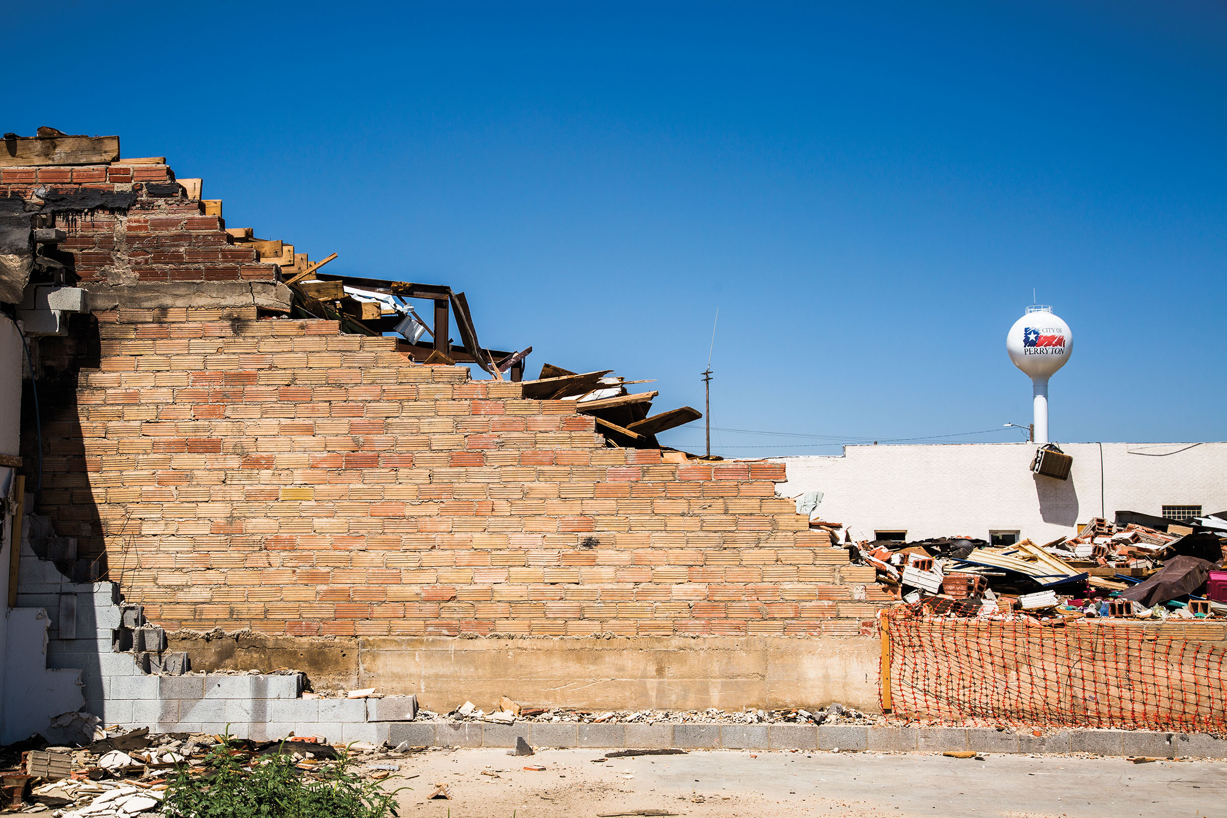A damaged brick wall with other rubble and a white water tower in the background