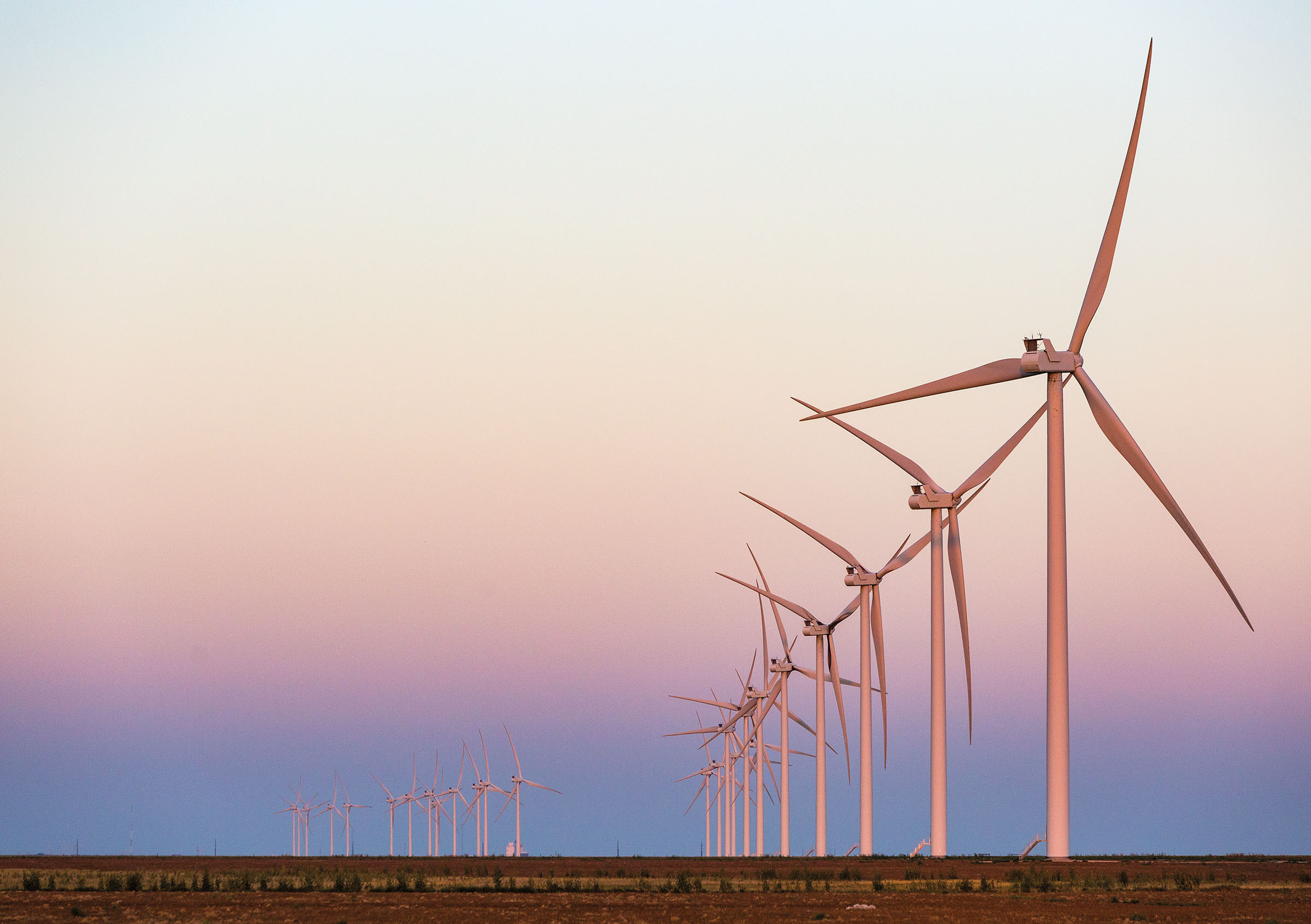 A line of tall white wind turbines in a blue and pink sunset backdrop