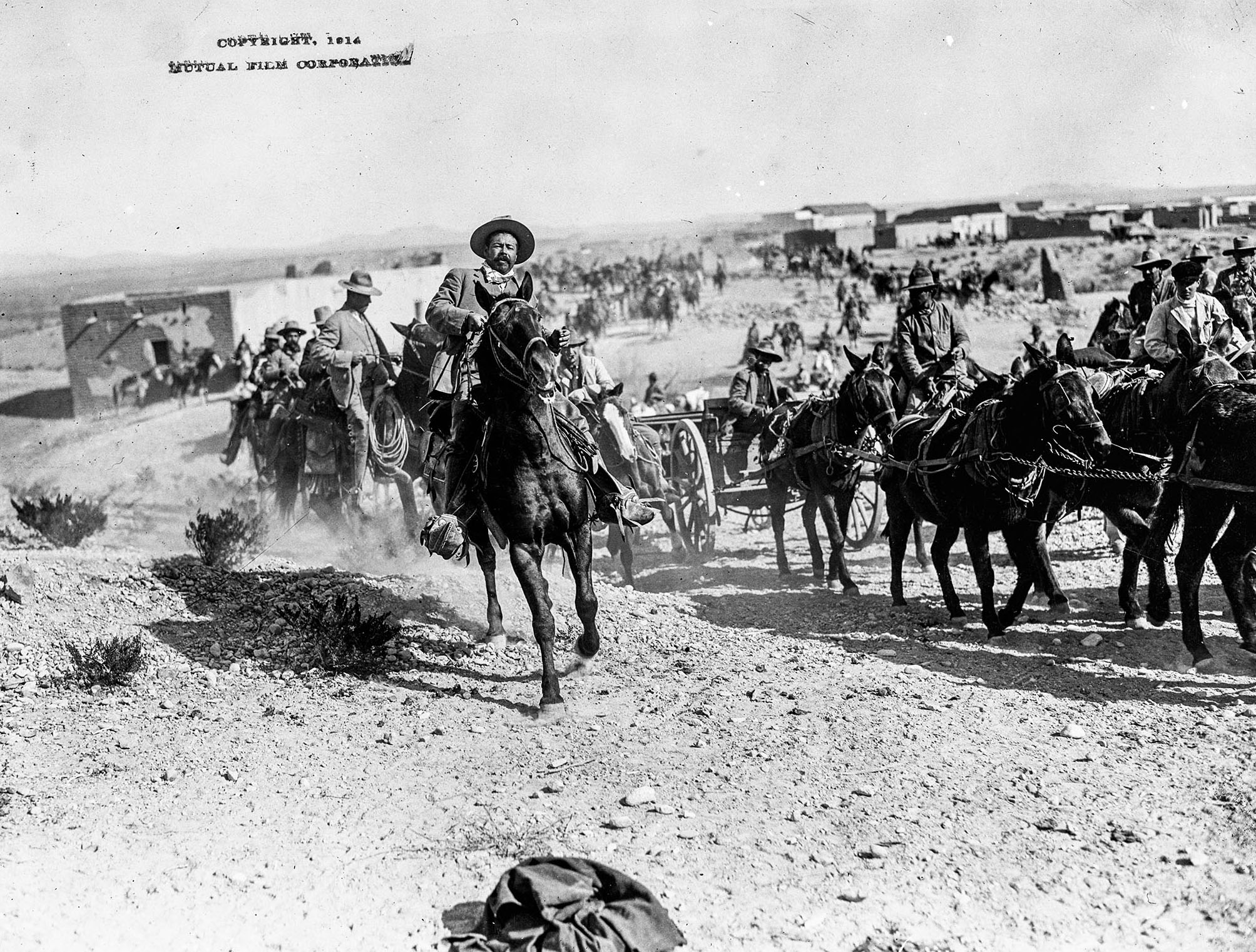A man in a cowboy hat rides a horse along with a large line of horses