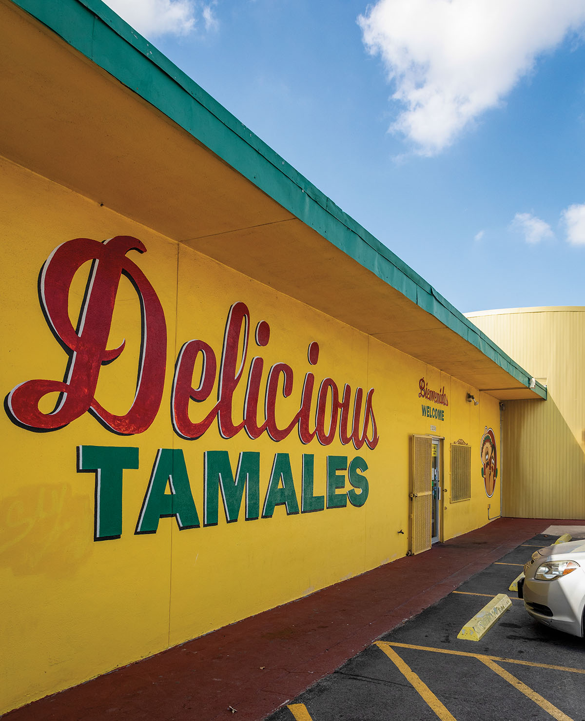The exterior of a bright yellow building painted to read "Delicious Tamales"
