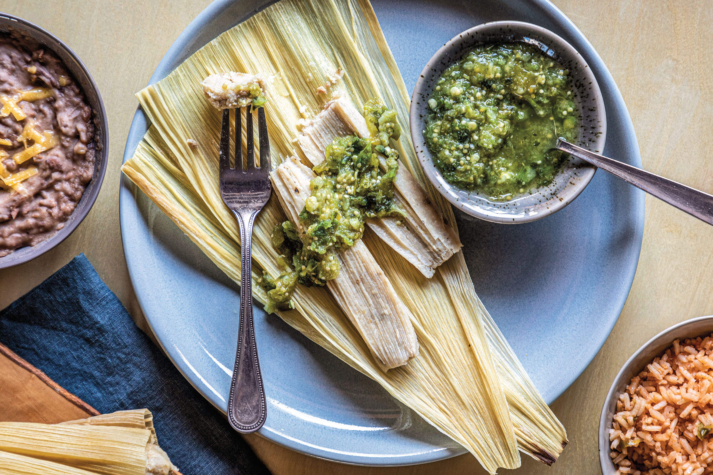 An overhead view of a blue plate of tamales served with green salsa