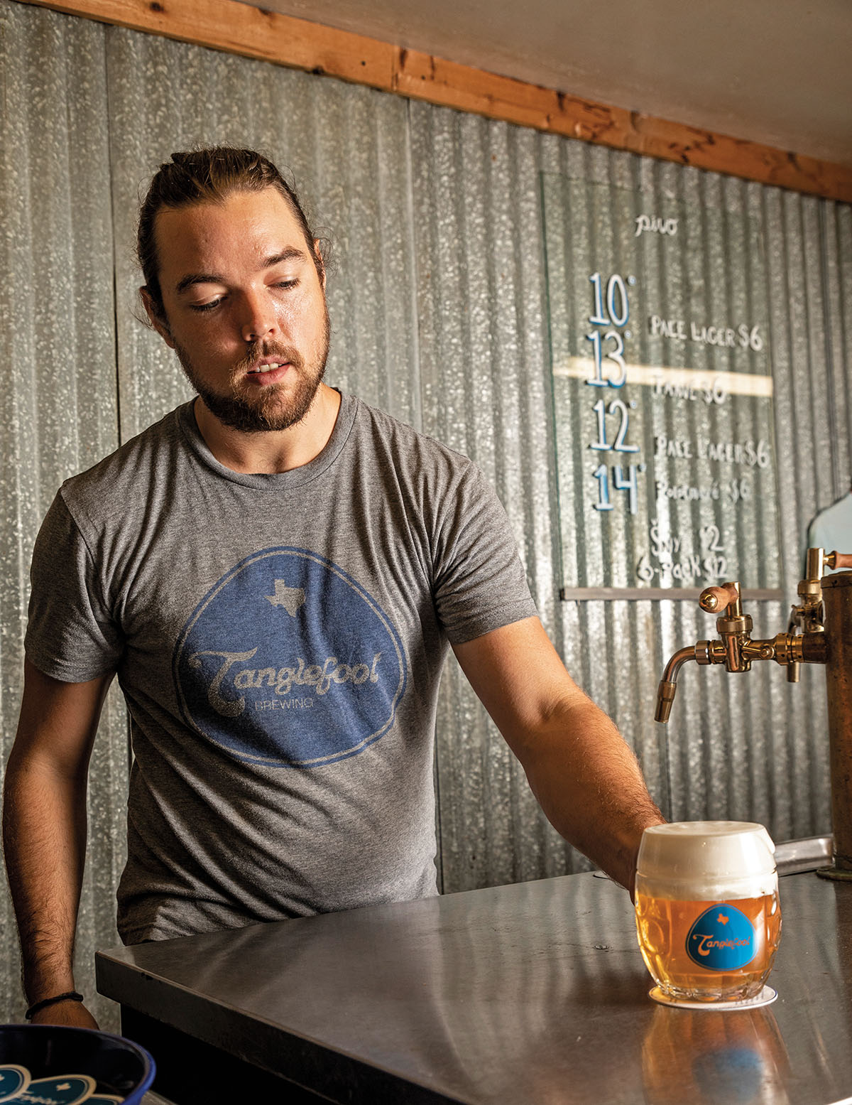 A man wearing a gray 'Tanglefoot Brewing' t-shirt holds a stein full of beer